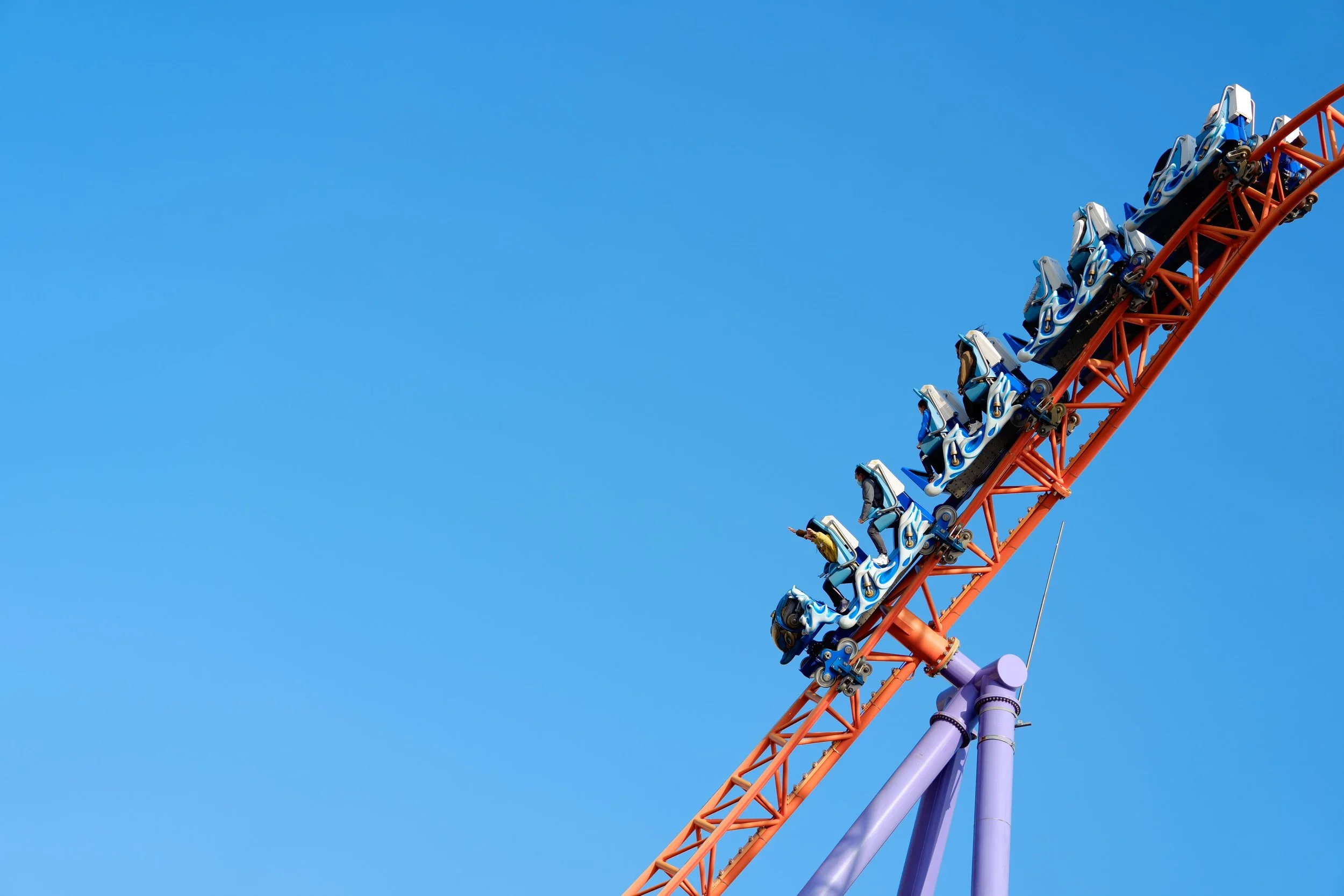 A roller coaster with riders on a steep downward track against a clear blue sky.