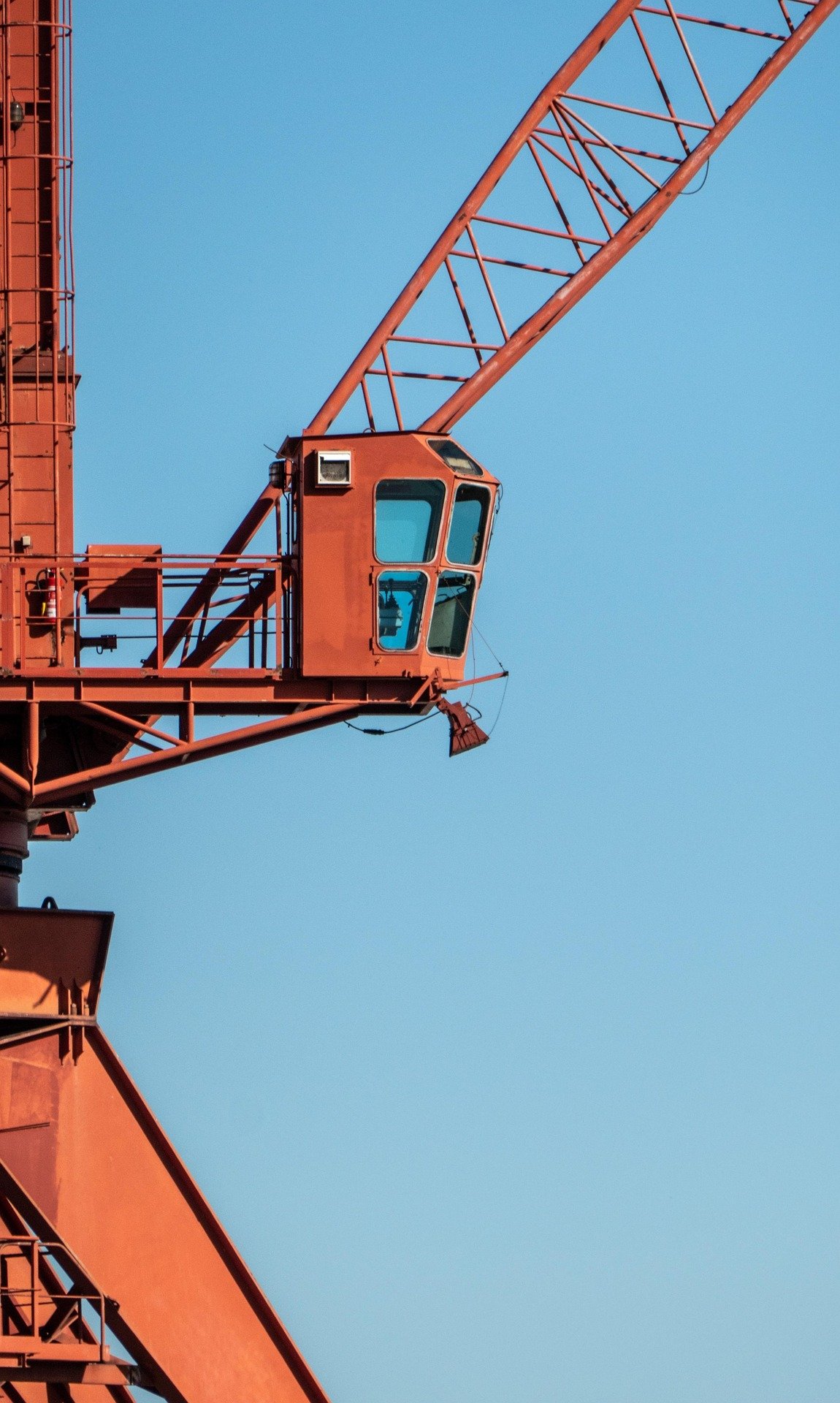 Close-up of the extensive orange metal framework of a construction crane against a bright blue sky.