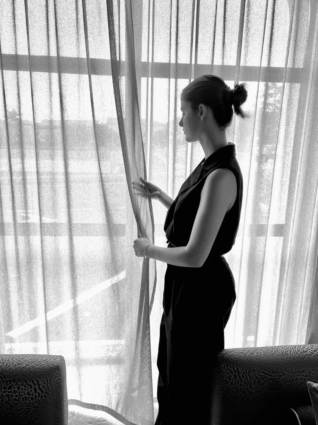 Marrit standing by a window with sheer curtains, looking at the fabric.