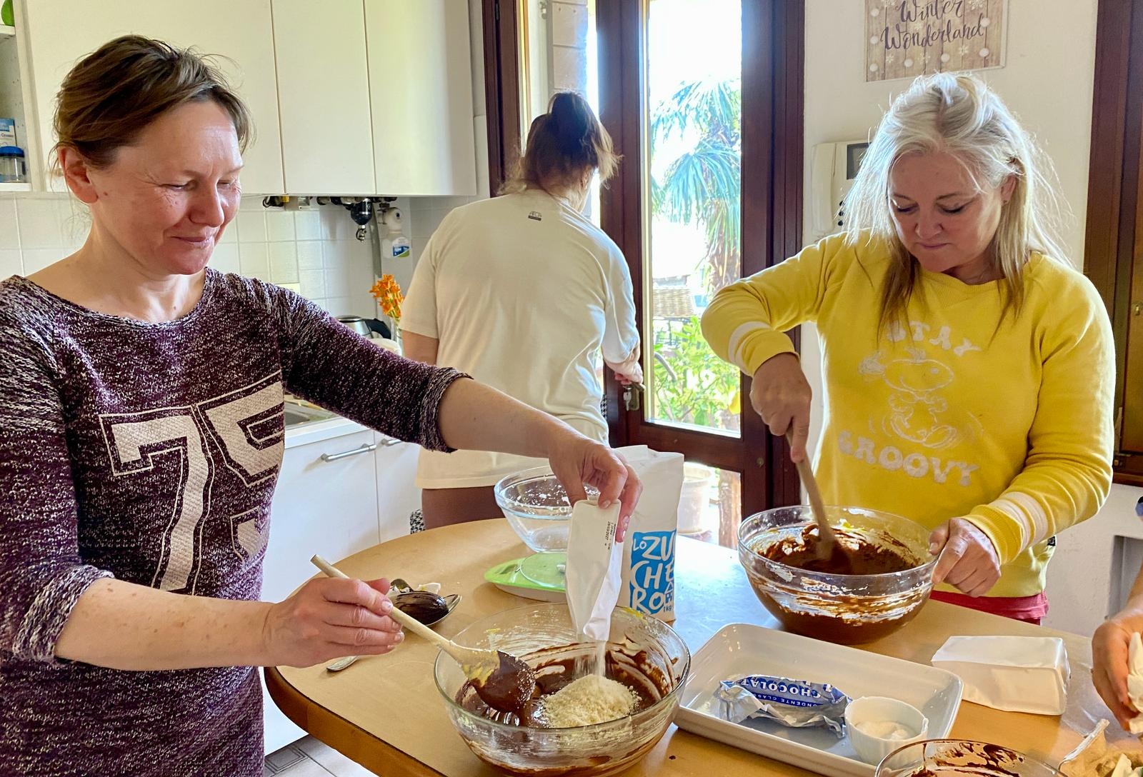 Two women mixing chocolate cake ingredients in a kitchen bowl.