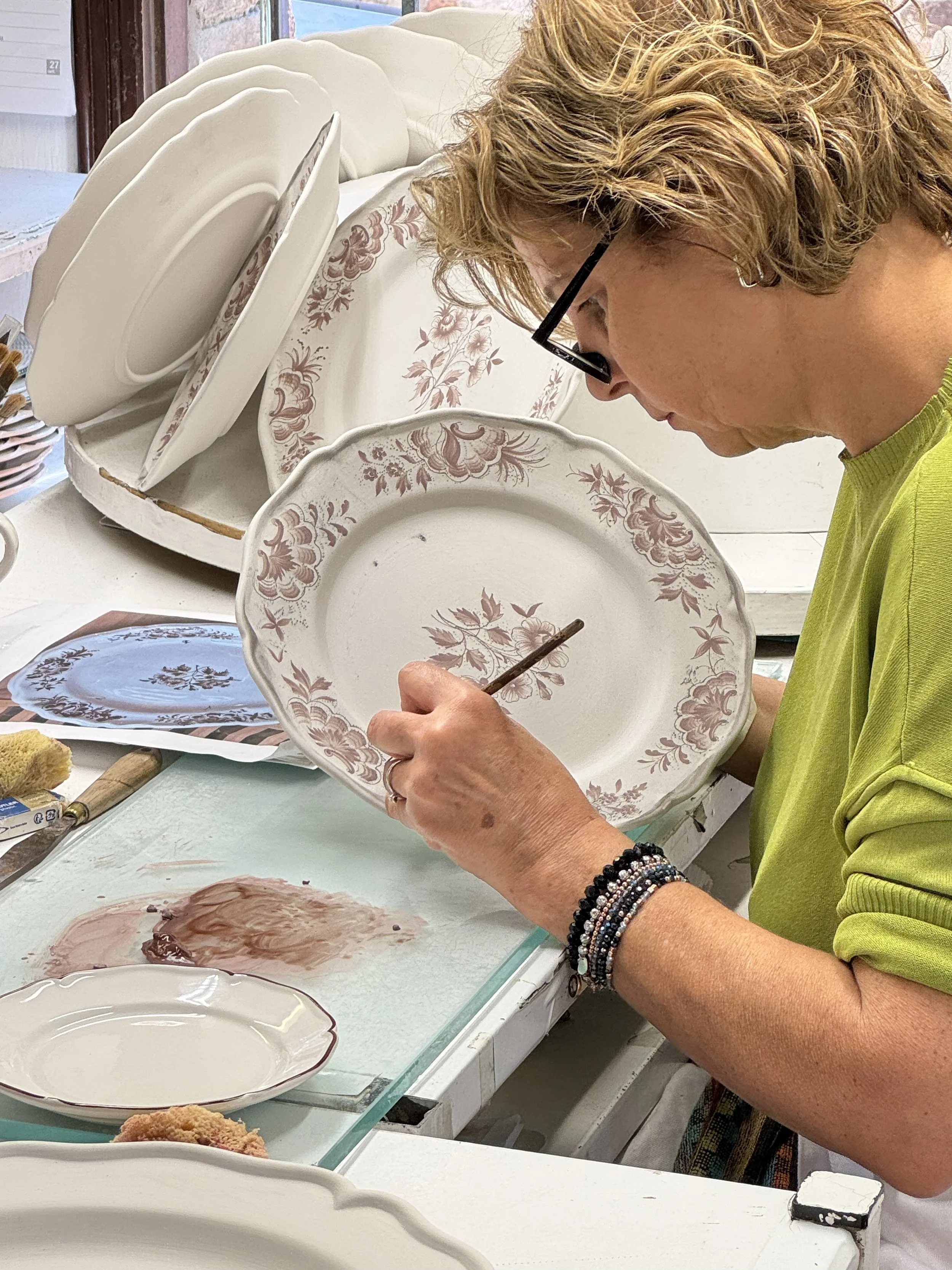 Member hand-painting a decorative ceramic plate with a brush.