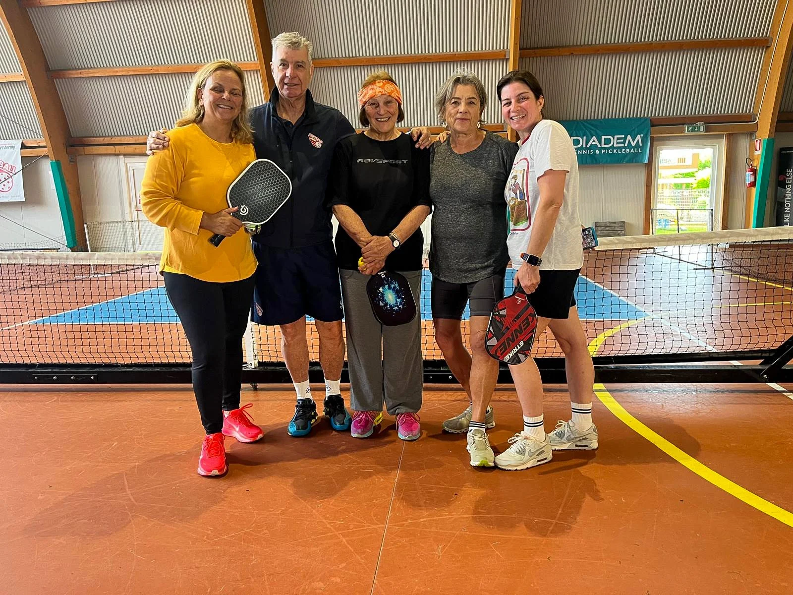 Smiling group of players holding pickleball paddles on an indoor court.