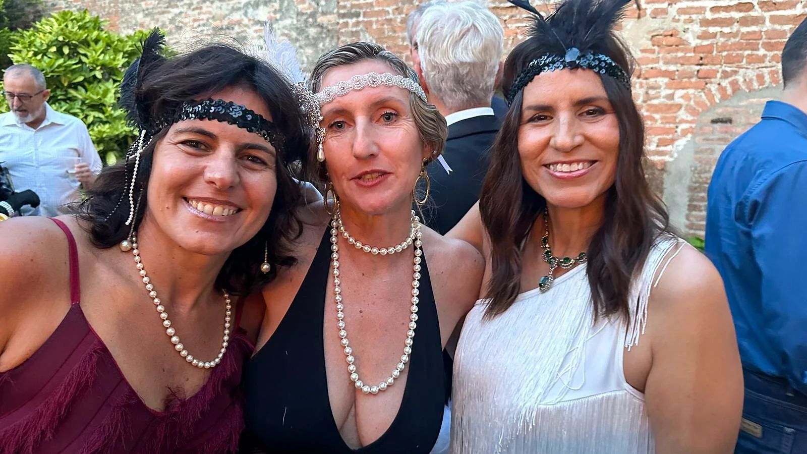 Three members smiling in 1920s themed headbands and pearl necklaces.