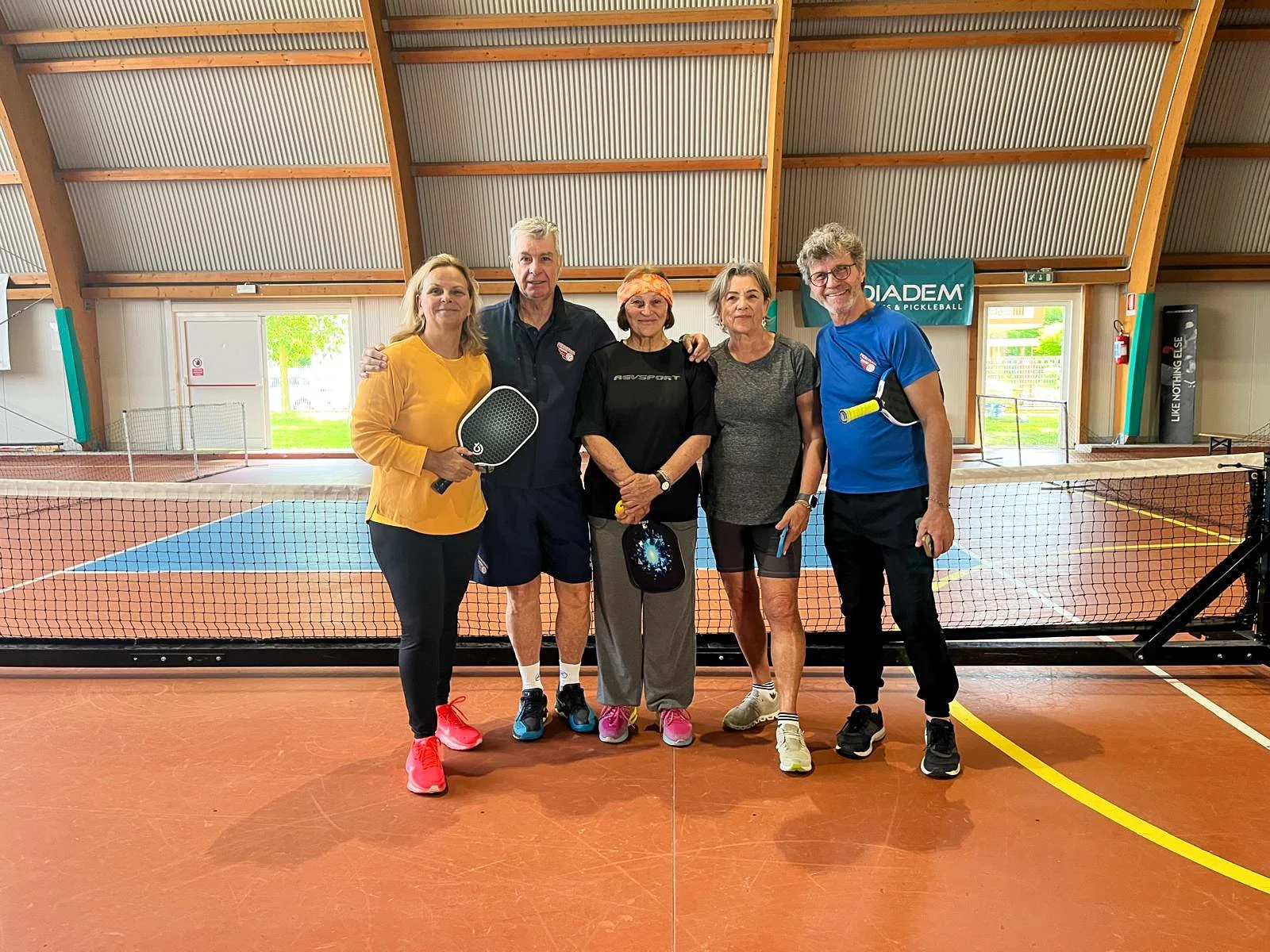 Group of members posing with pickleball rackets on an indoor court.
