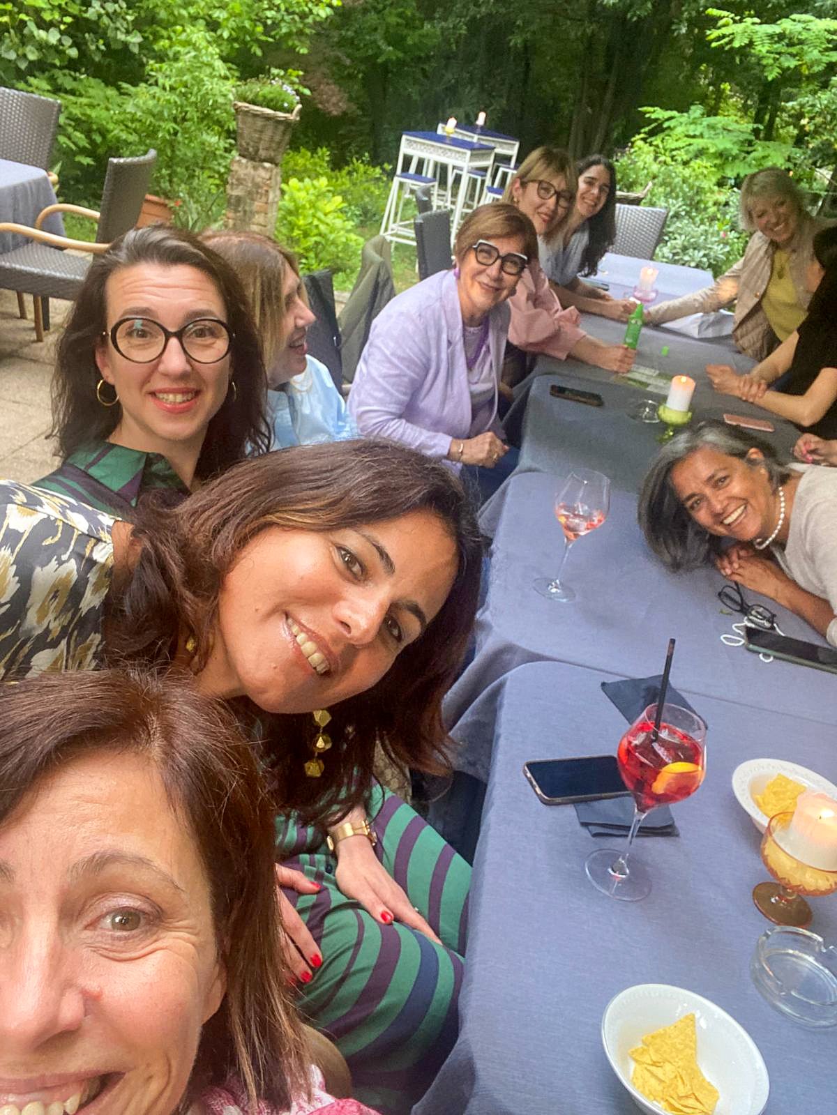 Members chatting over spritz and drinks at a long garden table.