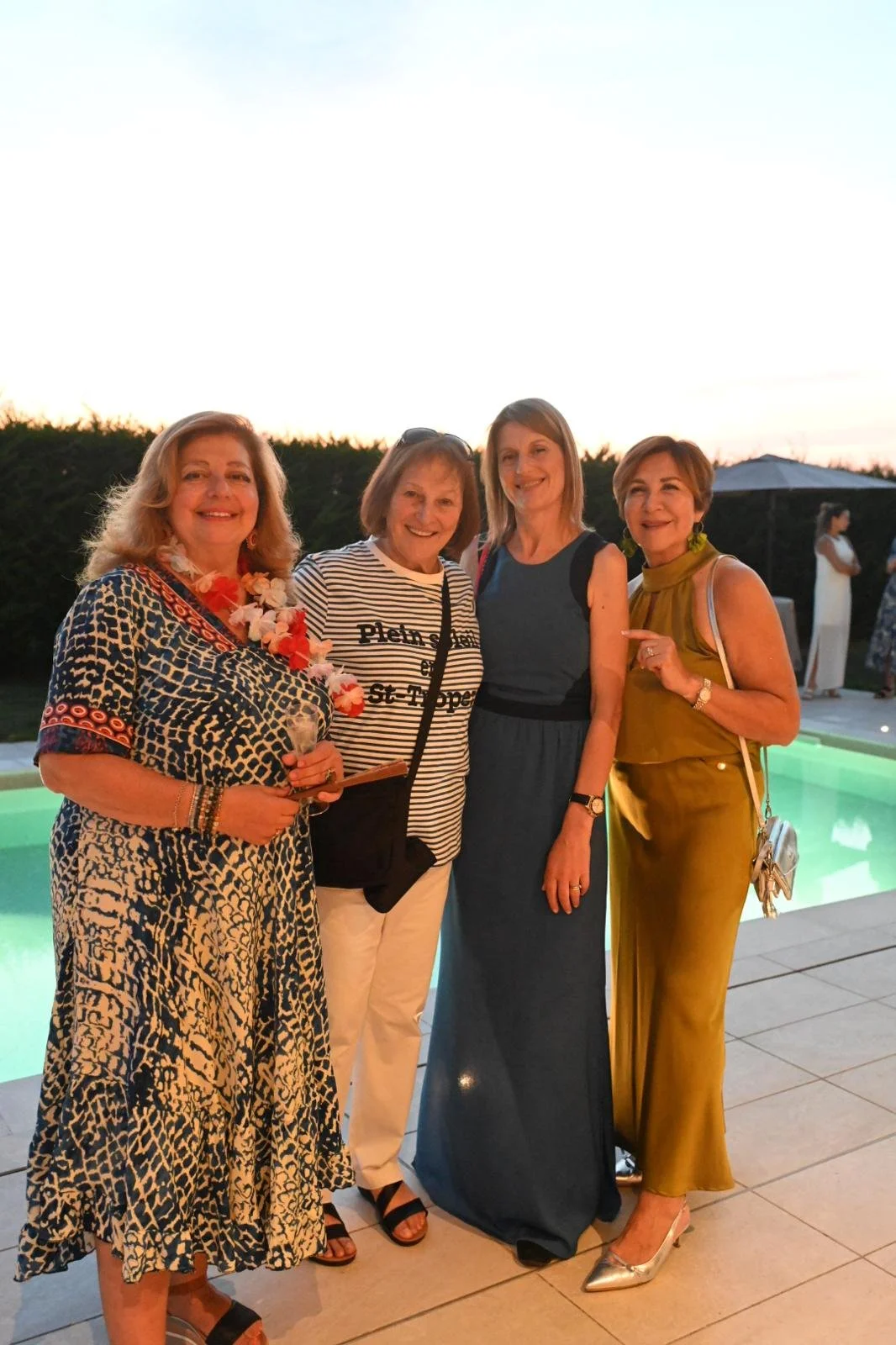 Four women posing outdoors next to a swimming pool in summer dresses.