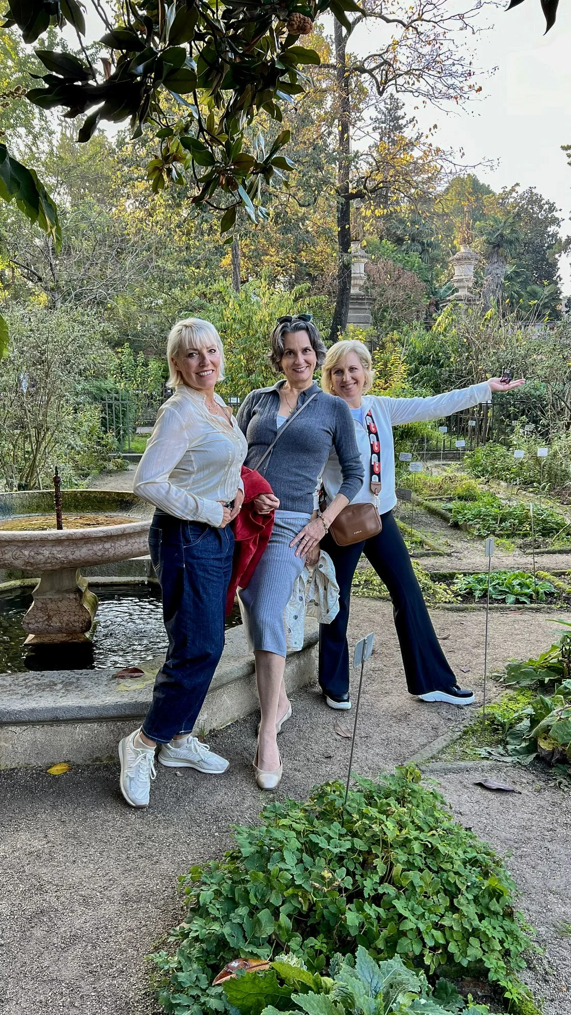 Three members posing near a stone fountain in a botanical garden.
