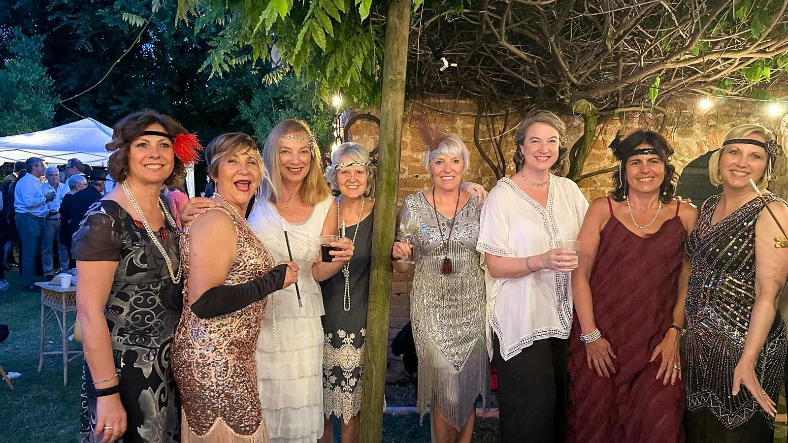 Seven women posing together in 1920s flapper dresses at a theme party.