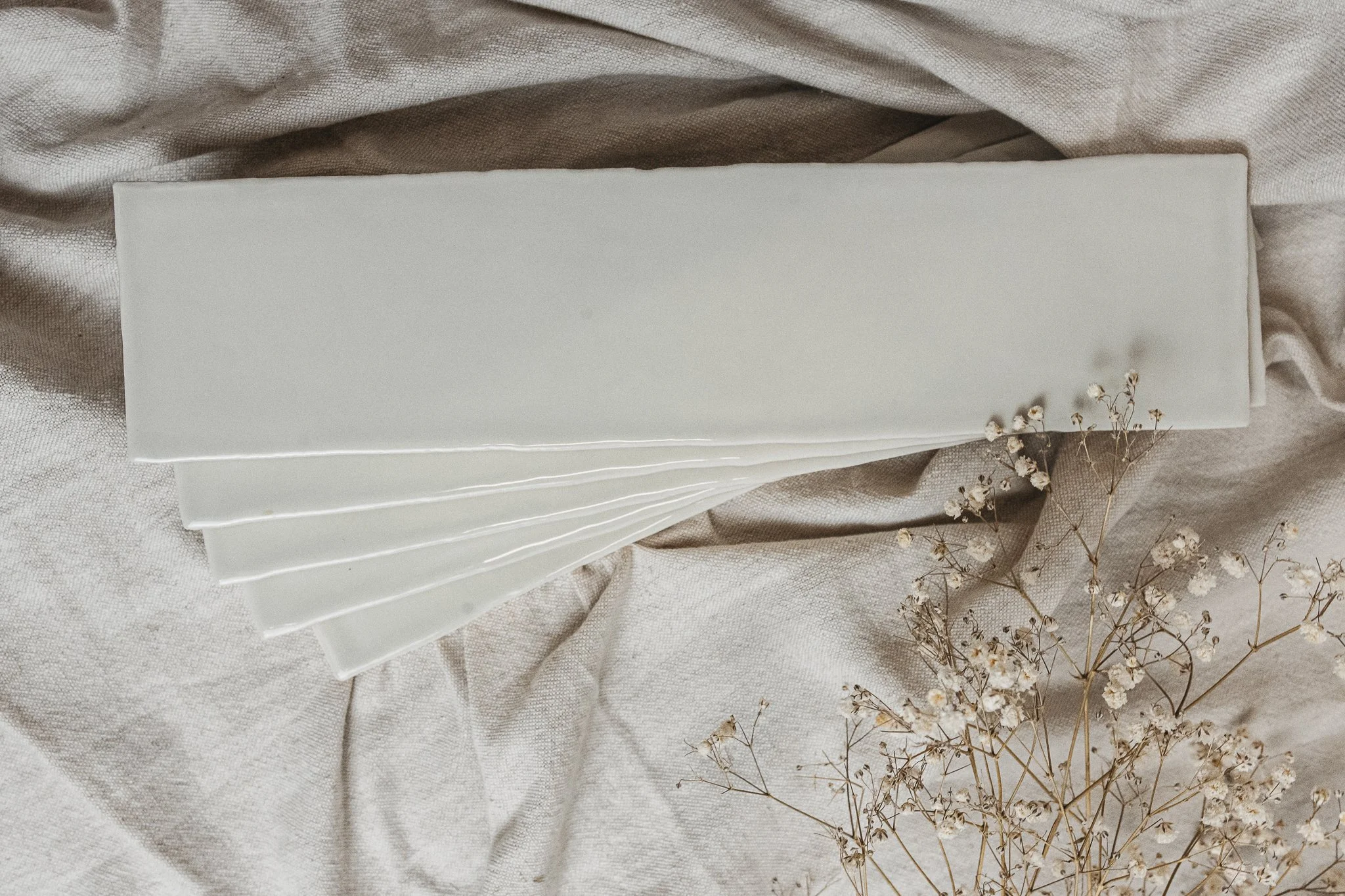 White paper napkins arranged in a fan shape on beige fabric, with sprigs of small white flowers nearby.