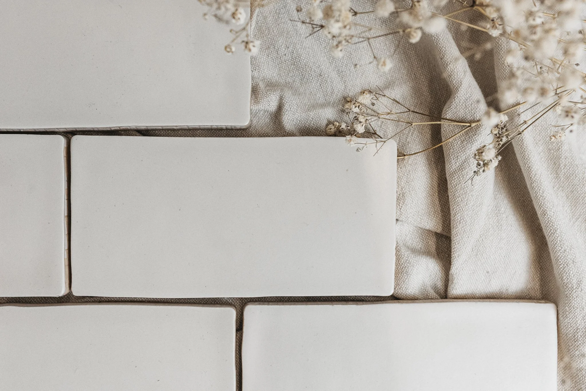 Close-up of a tiled surface with white tiles, beige fabric, and dried flowers.