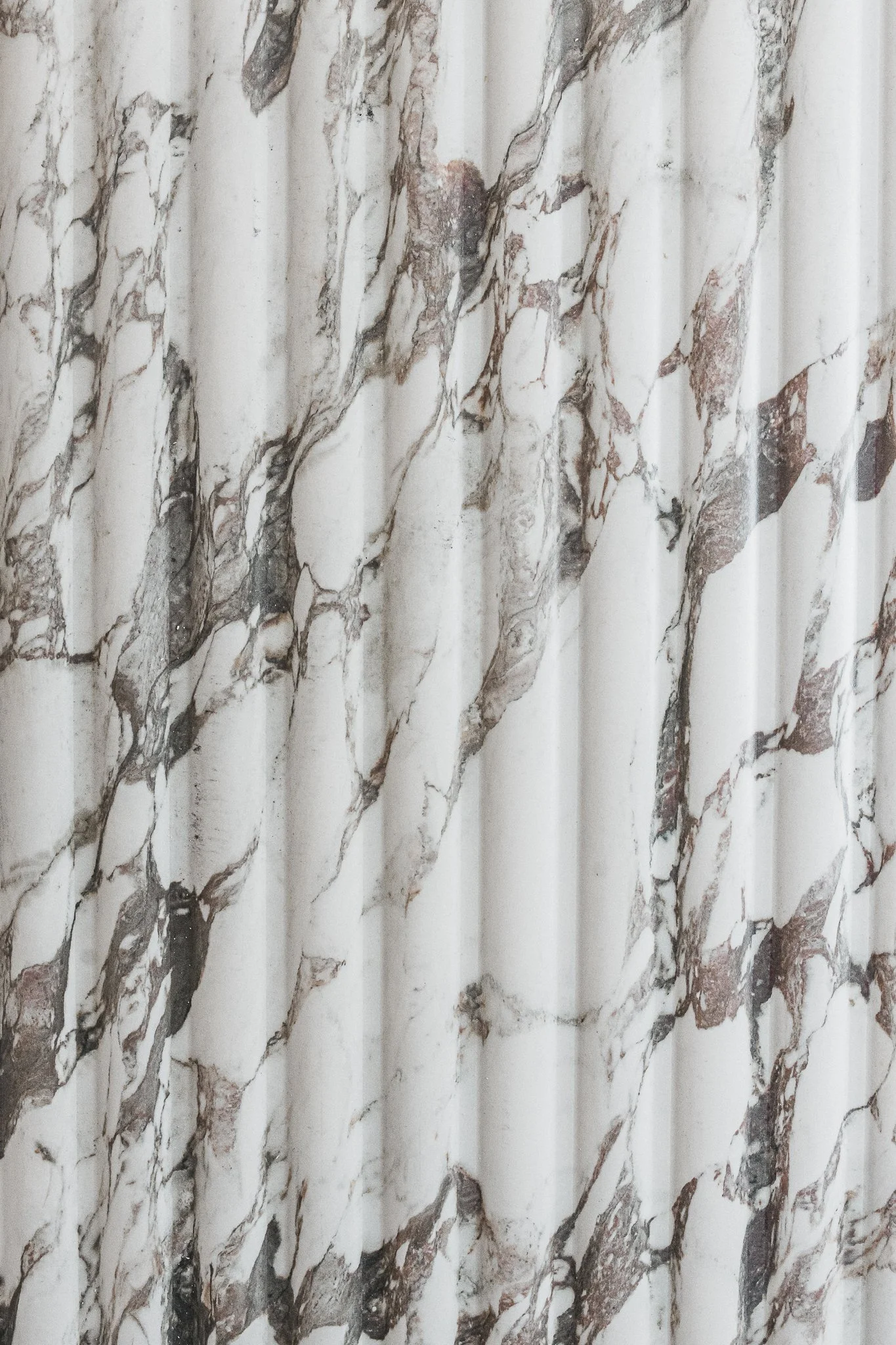 Close-up of a marble or stone surface with a white background and brown, gray, and black veining.