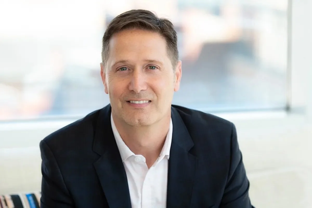 Professional man in business attire smiling at the camera in an office setting.