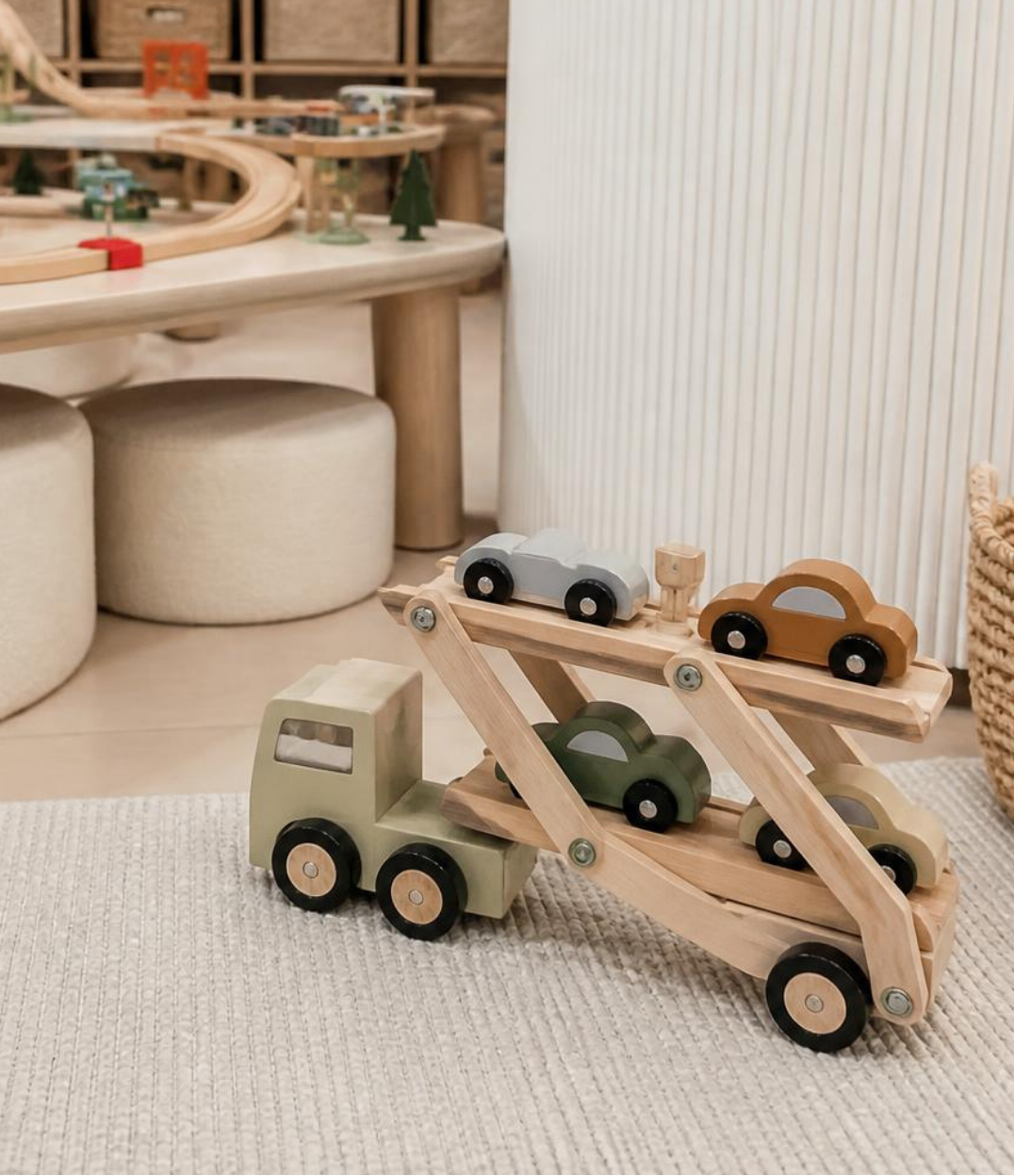 Wooden toy tow truck with several wooden cars on its ramp in a playroom.