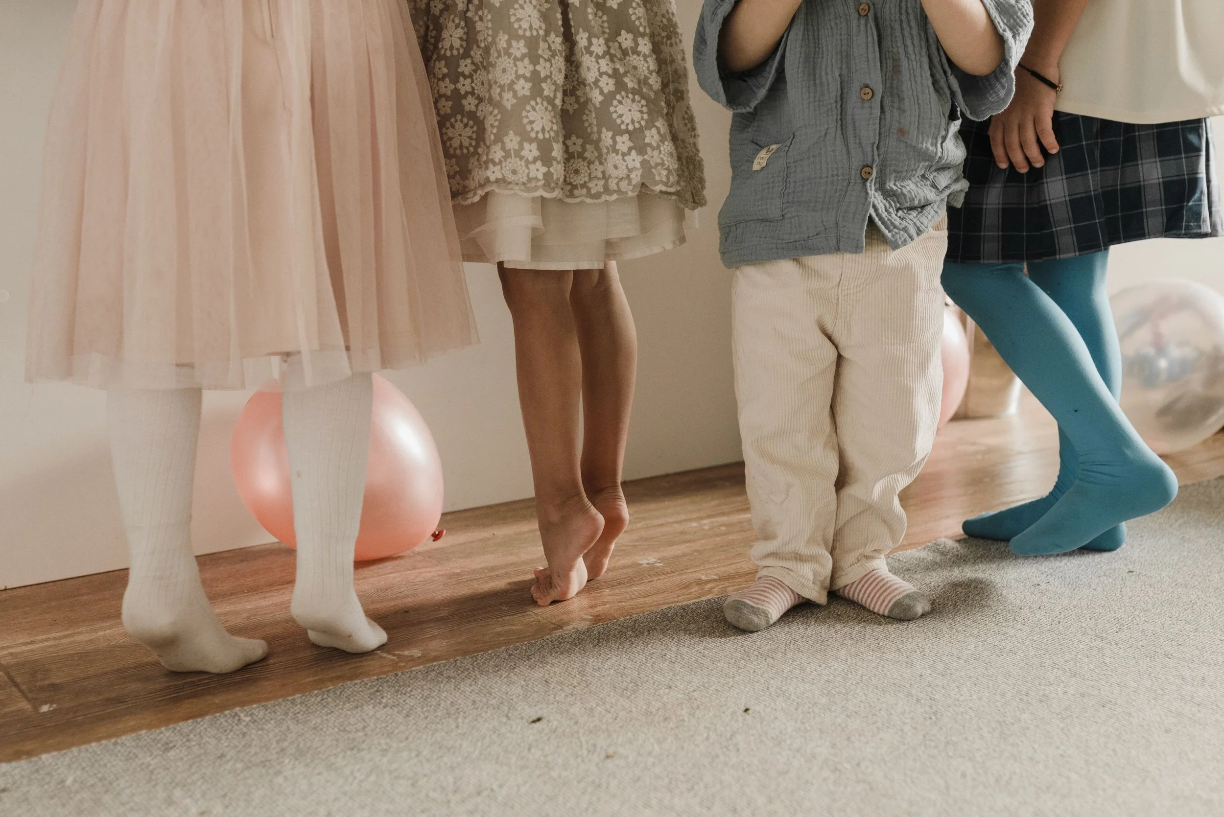 Children standing in a line with mannequins dressed in various outfits, one in pink tights with white socks, another in beige shorts, and others in casual and colorful clothing.