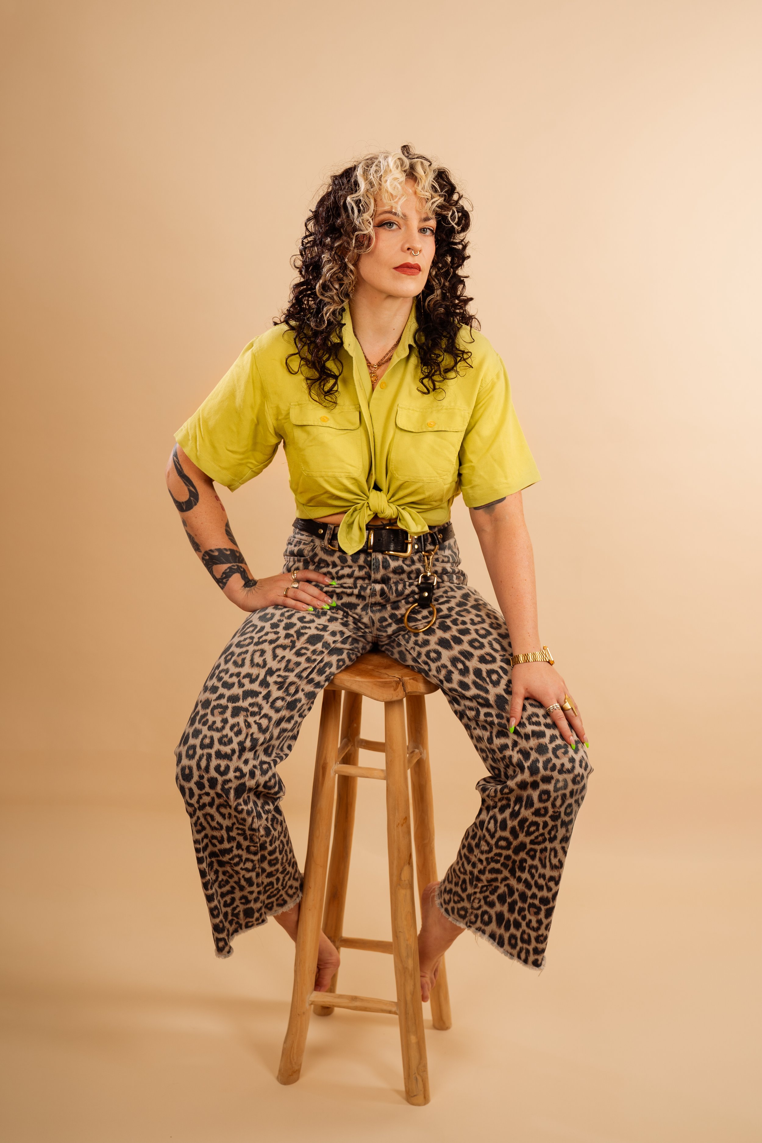 Portrait of Constanze Baumfrisch sitting on a wooden stool, wearing a lime green shirt and leopard-print trousers.