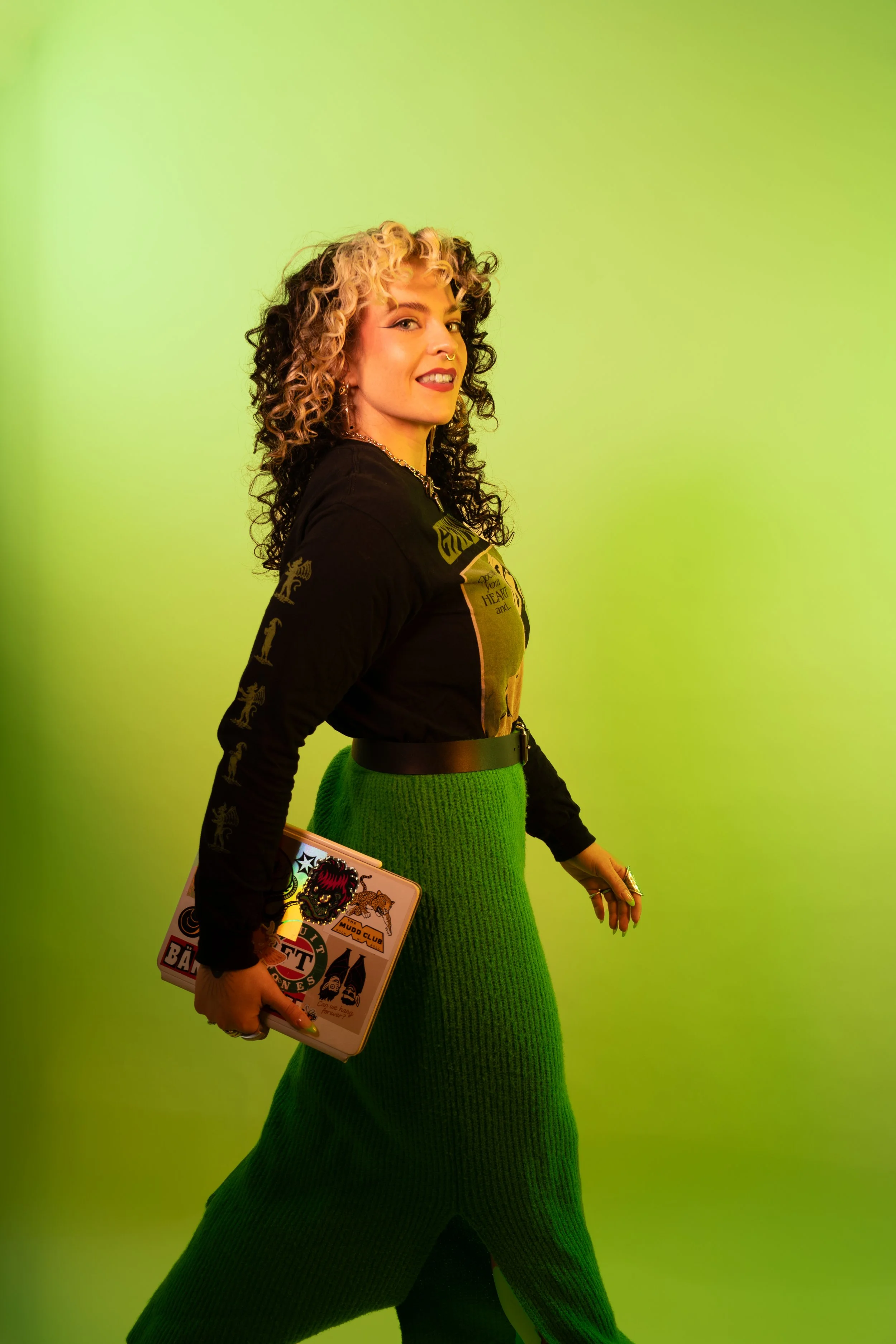 Constanze Baumfrisch walking in front of a bright green background, carrying a sticker-covered iPad.