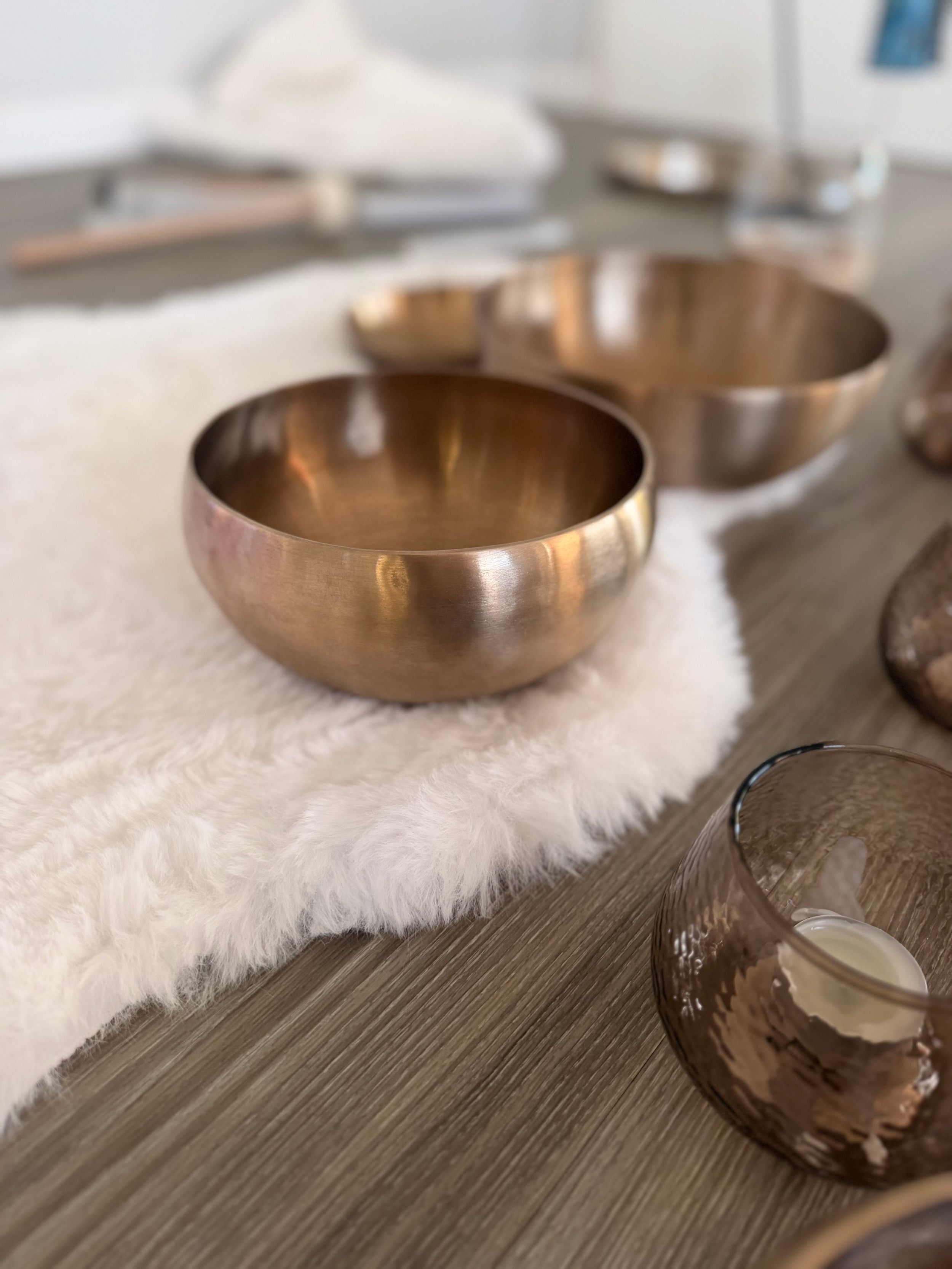 Zwei goldene Schalen auf einem weißen Teppich, in der Nähe eines Glases mit einer Kerze, auf einem Holztisch.