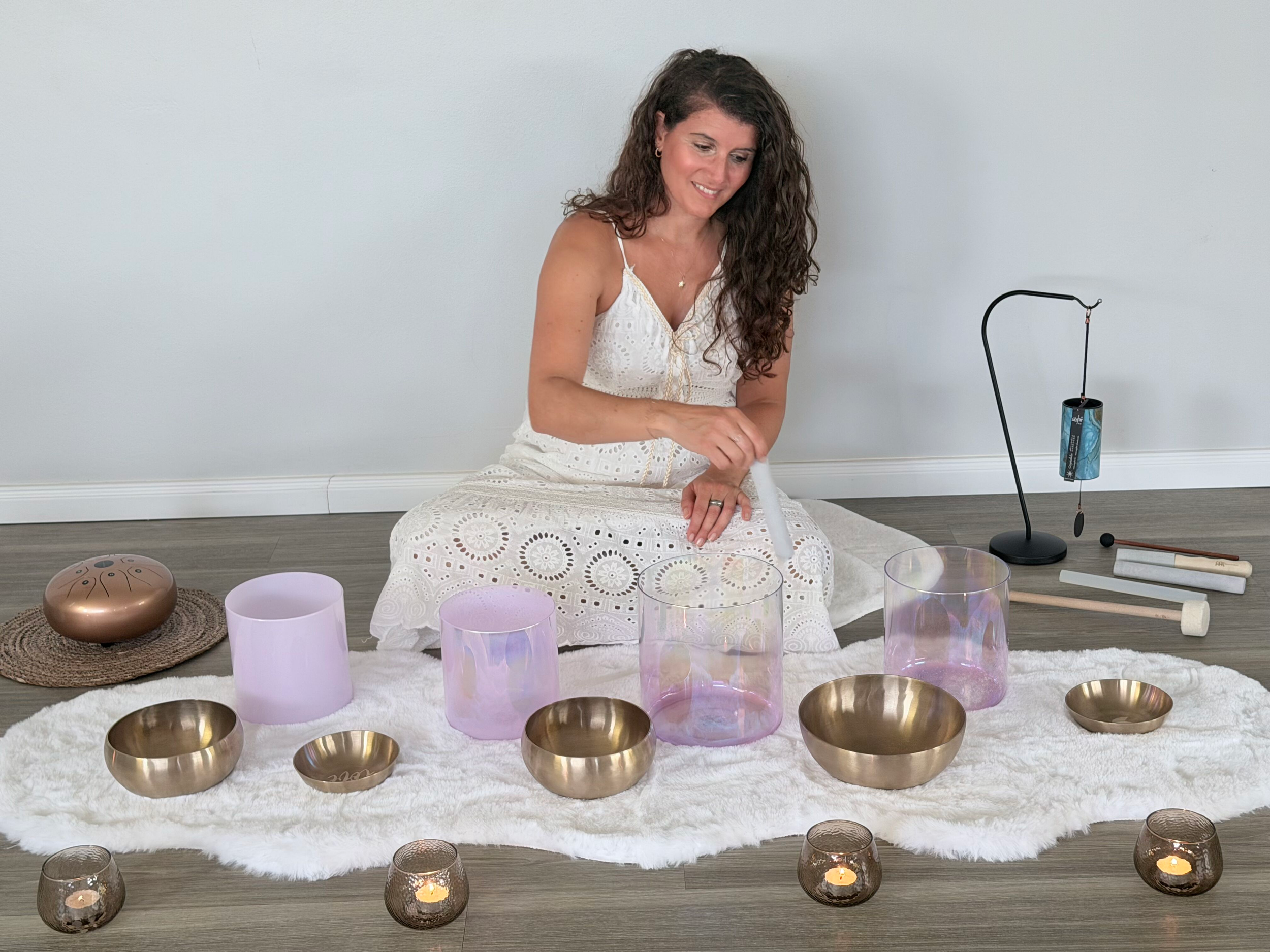 Eine Frau sitzt auf einem weißen Teppich, umgeben von Muschelschalen, Glaskerzen und anderen spirituellen Gegenständen, während sie scheinbar eine Meditation oder Zeremonie durchführt.
