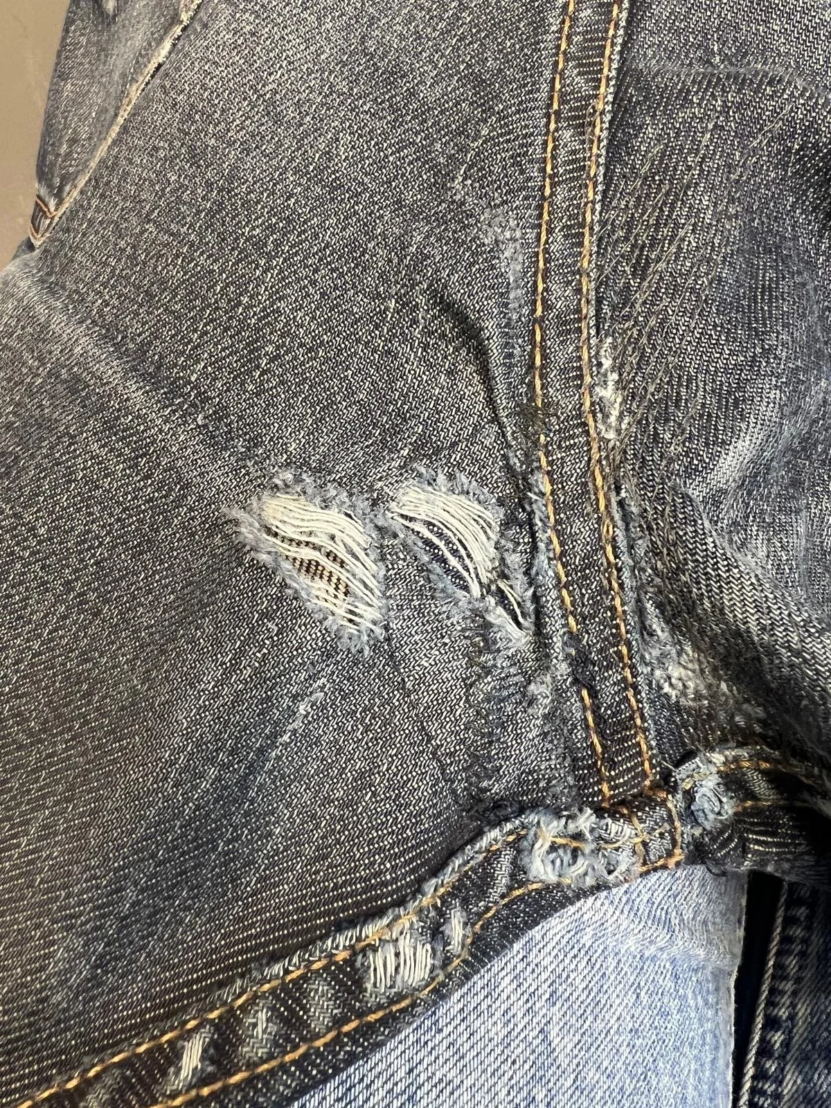 Detalj av ett par slitna blå jeans, visar trasiga hål i tyget och synliga innermesh.