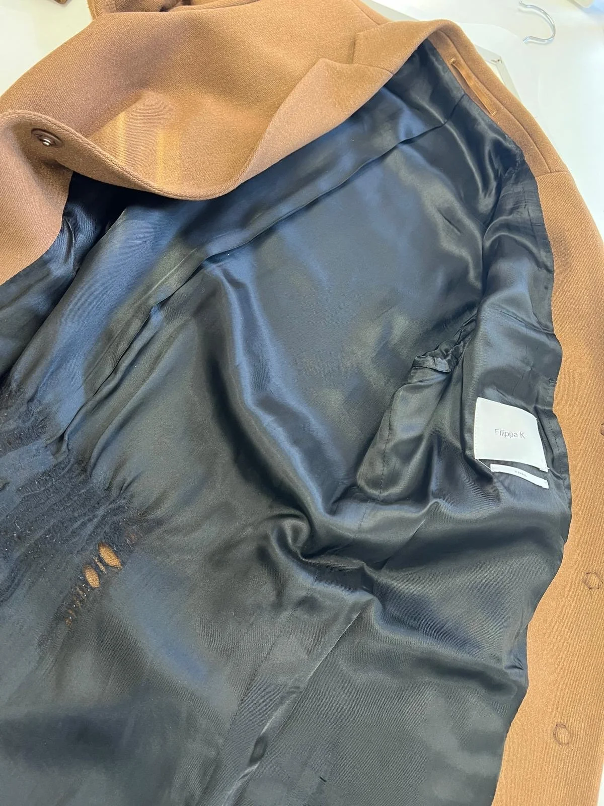 Insidan av en svart kappa med en etikett där det står 'Ellipa K' syns, liggande på en brun yta.