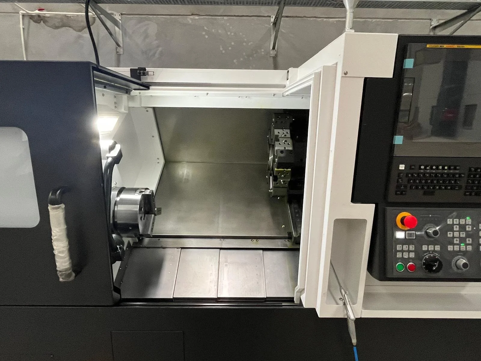 A CNC machine with an empty work area, control panel with buttons, switches, and display, and a protective cover on top.