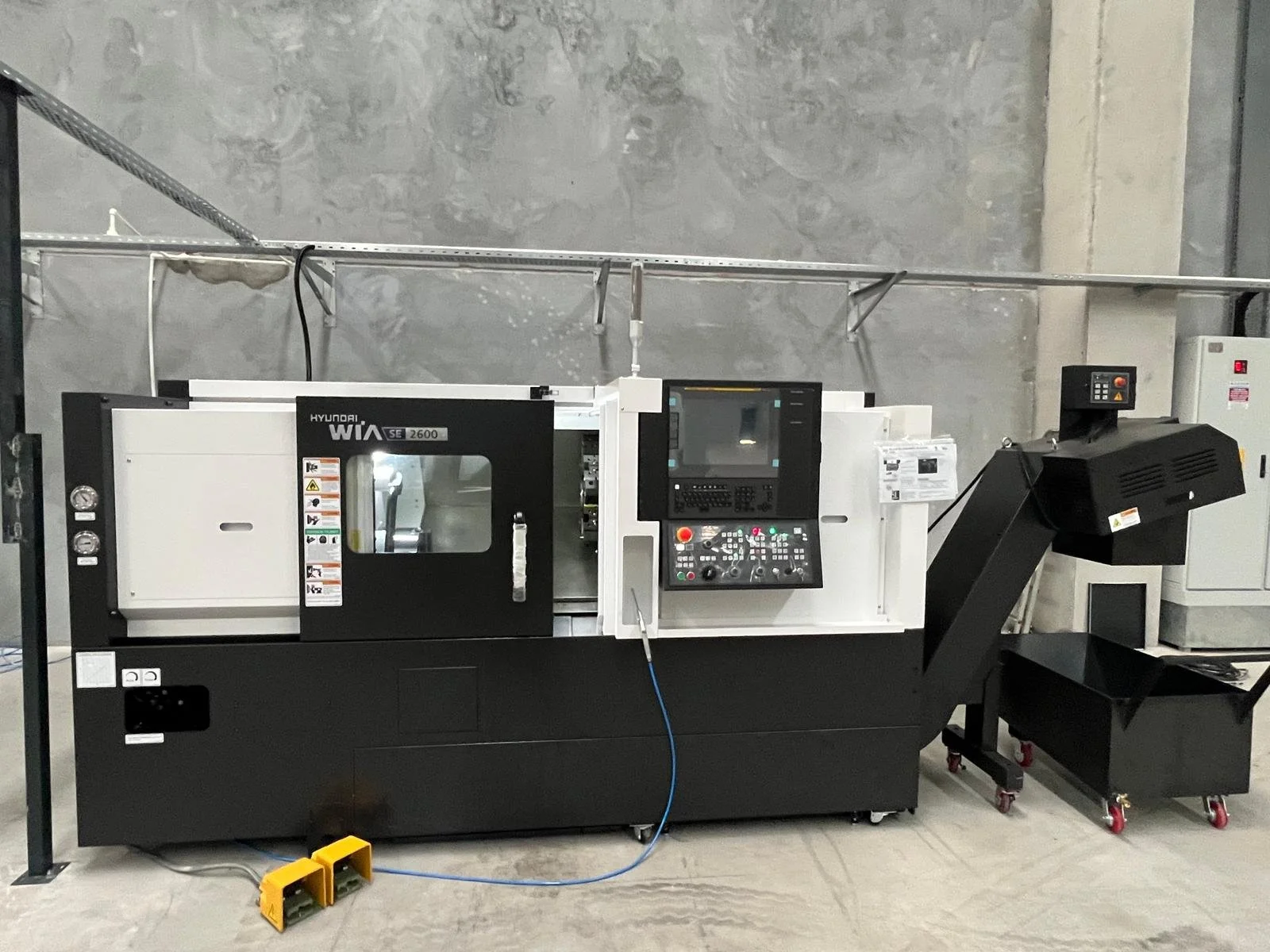 A Hyundai WIA SE 2600 CNC machine in a workshop setting with control panel and safety warnings.