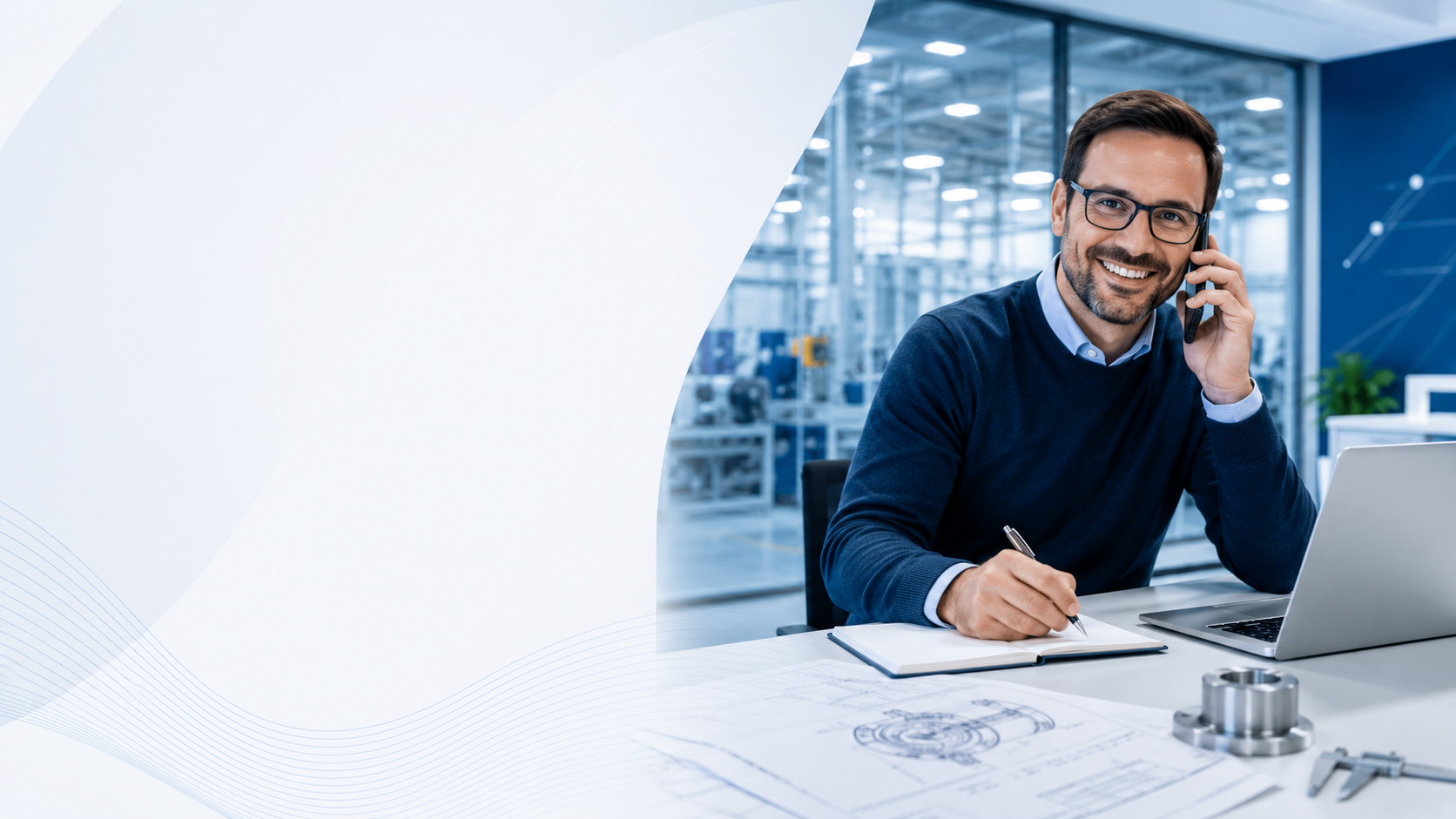 Man in glasses smiling and talking on a cellphone at a desk in a modern office or manufacturing environment, with blue tones and technical drawings and machinery parts on the desk.