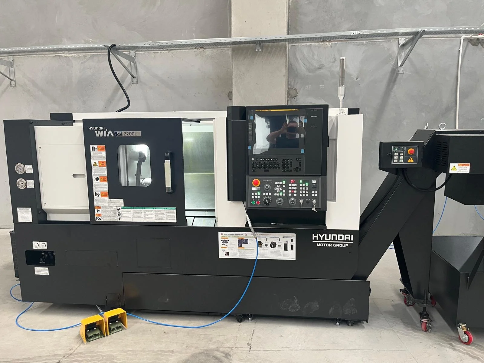 A Hyundai WIA CNC machine in a workshop with control panel and safety design, placed against a concrete wall.