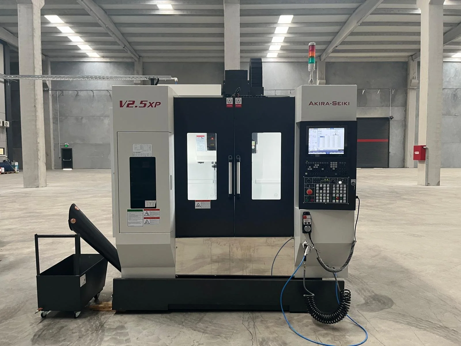 A CNC machine in a large, empty industrial space with concrete floors and support columns.