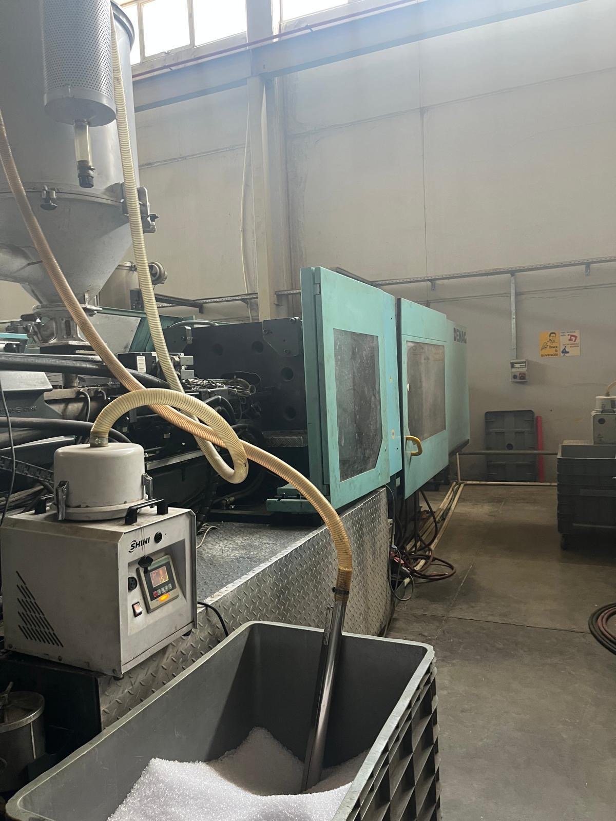 Industrial equipment and machinery in a factory setting, with a container of white granular material in the foreground.