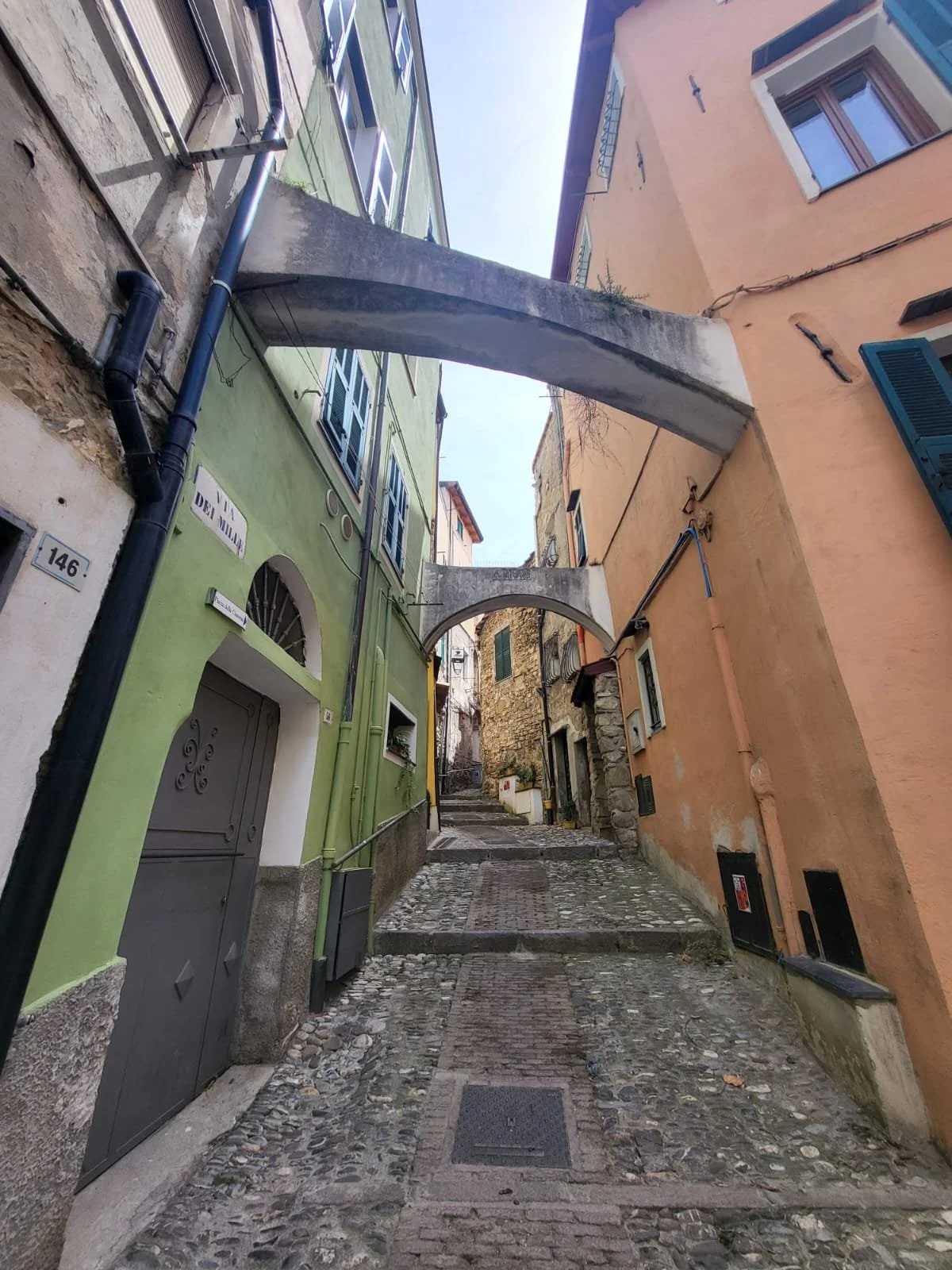 Narrow cobblestone alleyway lined with multi-colored buildings, featuring arches, windows with shutters, and a slight incline.