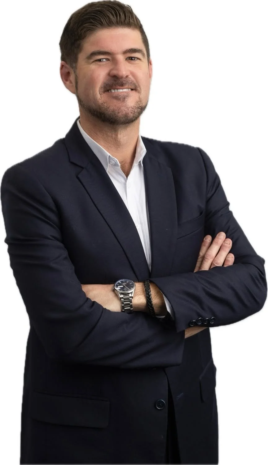 A man with dark hair and a beard, wearing a dark suit and a white shirt, crossing his arms and smiling, against a plain white background.