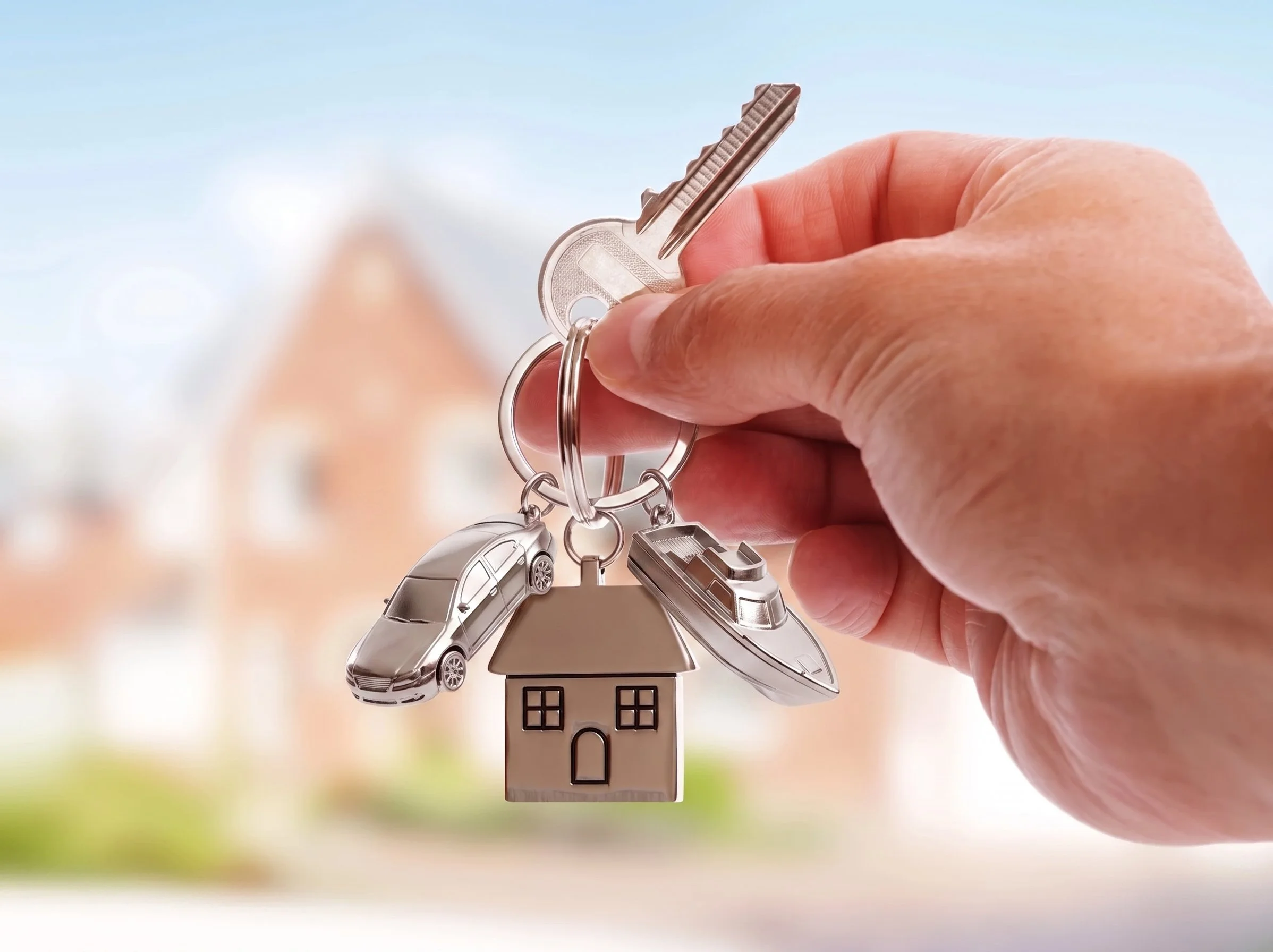 A person holding a keychain featuring a house, a car, a plane, and a house with a swing outside.