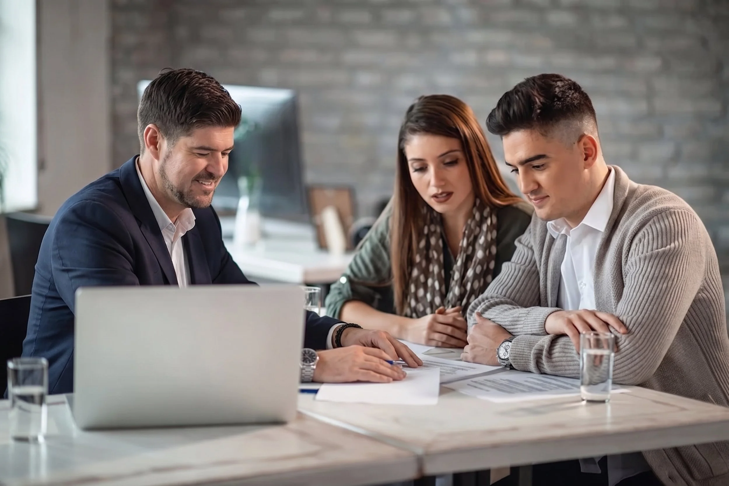 Three people examine documents at a meeting table in a modern office setting.