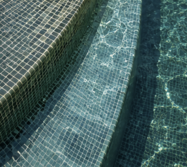 Close-up of swimming pool steps with blue mosaic tiles, with sunlight reflecting on the water.