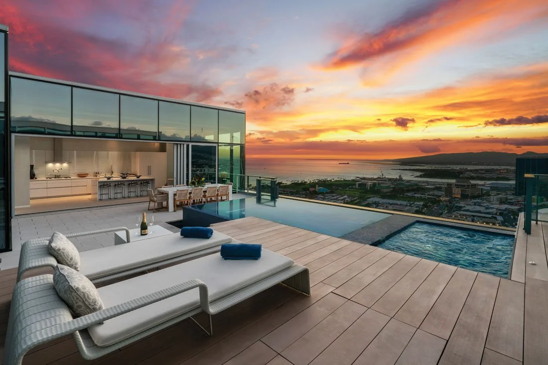 Luxury rooftop pool and outdoor lounge area at sunset with city, harbor, and mountain views.