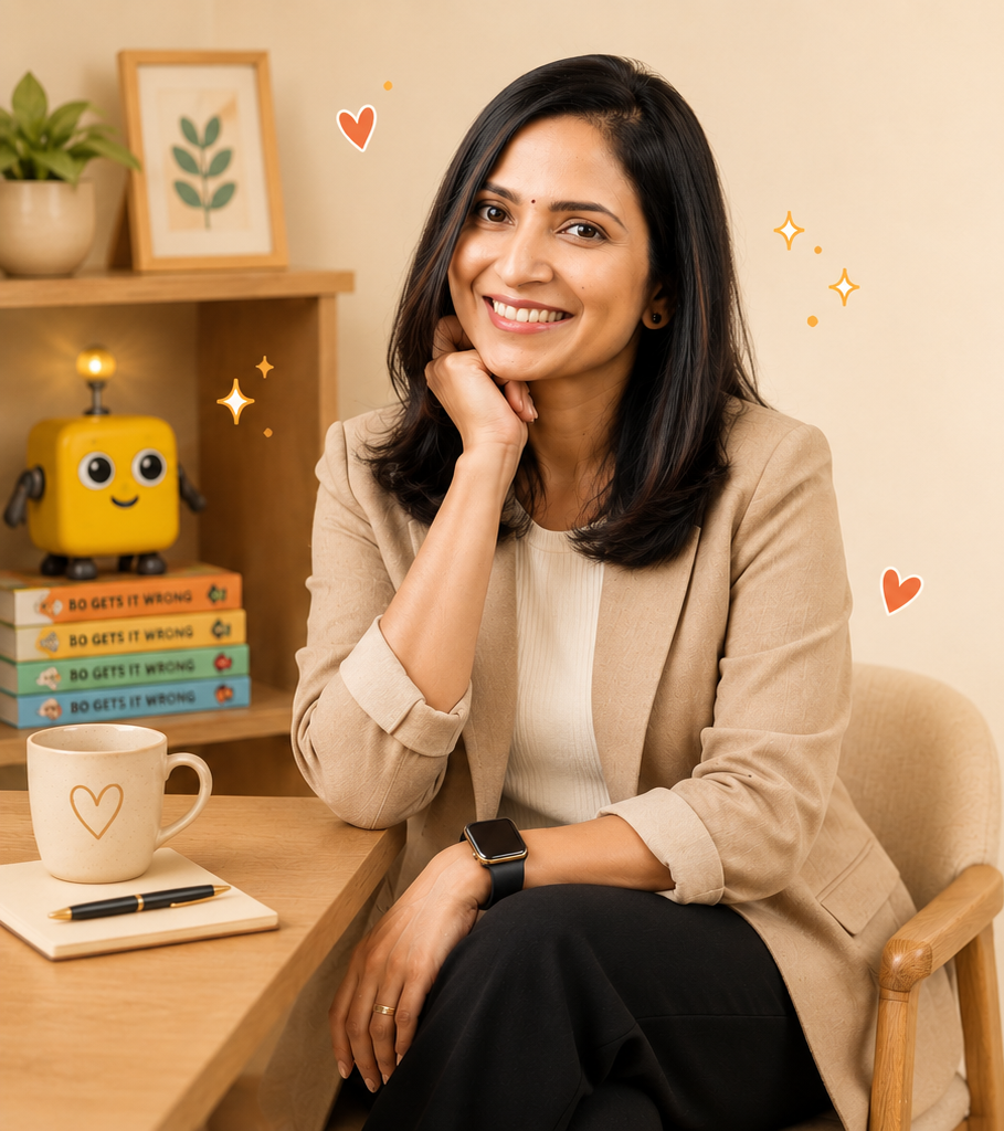 A smiling woman with shoulder-length black hair sitting at a wooden table in an indoor setting. She rests her chin on her hand and wears a beige blazer, a light-colored top, and a smartwatch. On the table, there is a mug with a heart design, a notebook, and a pen. In the background, a shelf holds potted plants, framed art featuring leaves, a yellow robot toy, and a stack of books titled 'Do Gets It Wrong'. Small decorative hearts and stars are overlaid in the image.