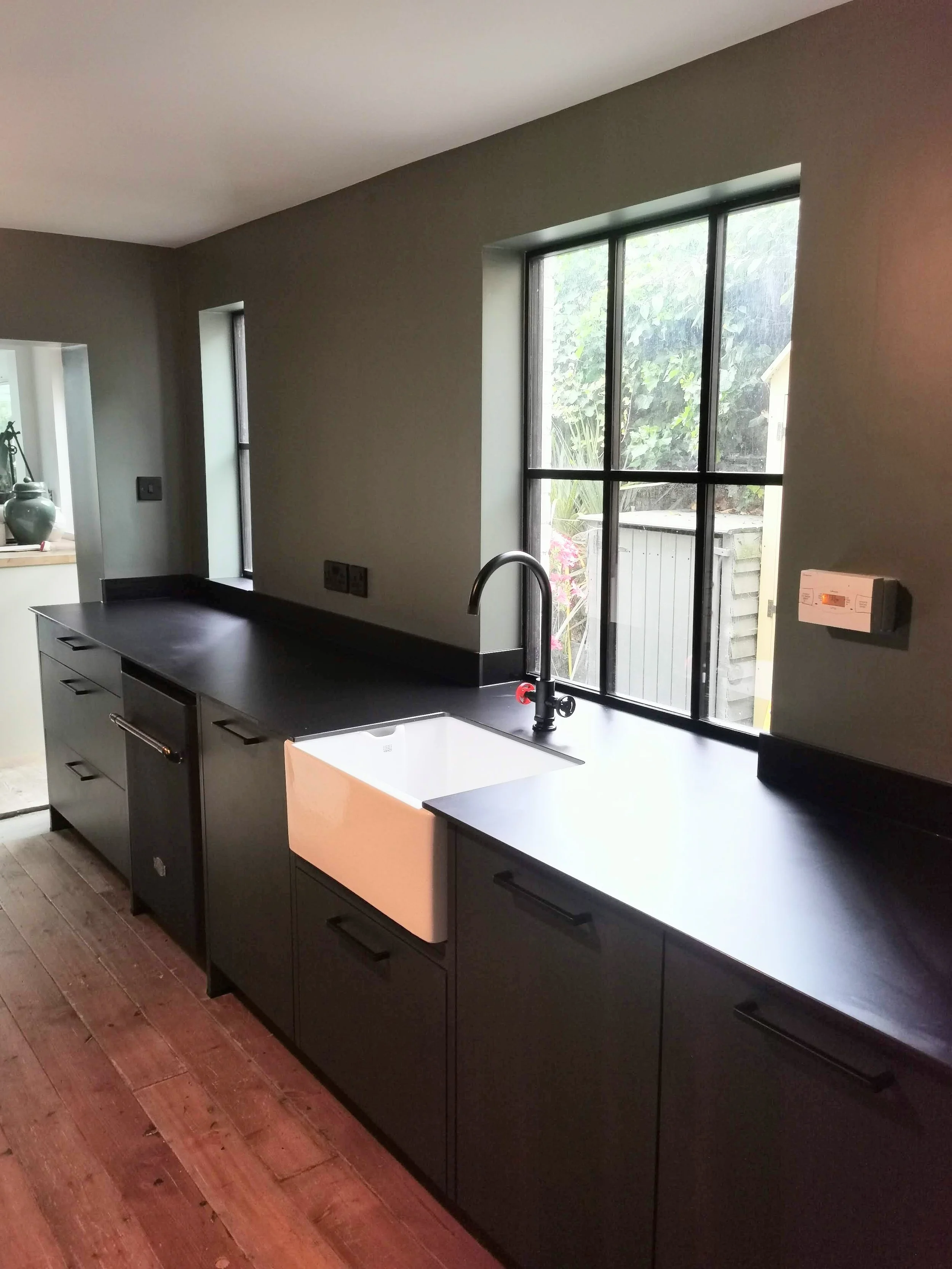 Painting in Stamford Modern kitchen with black cabinets, a white farmhouse sink, and large windows with a view outside, featuring wooden flooring.