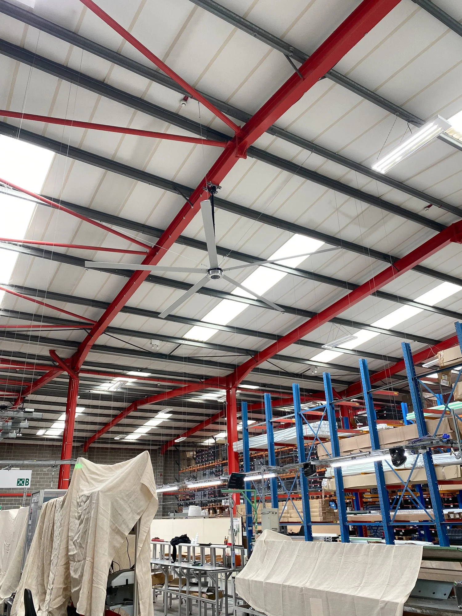 Interior of a large retail or warehouse store under construction with tall shelving units, a ceiling fan, and exposed ceiling beams and lighting fixtures.