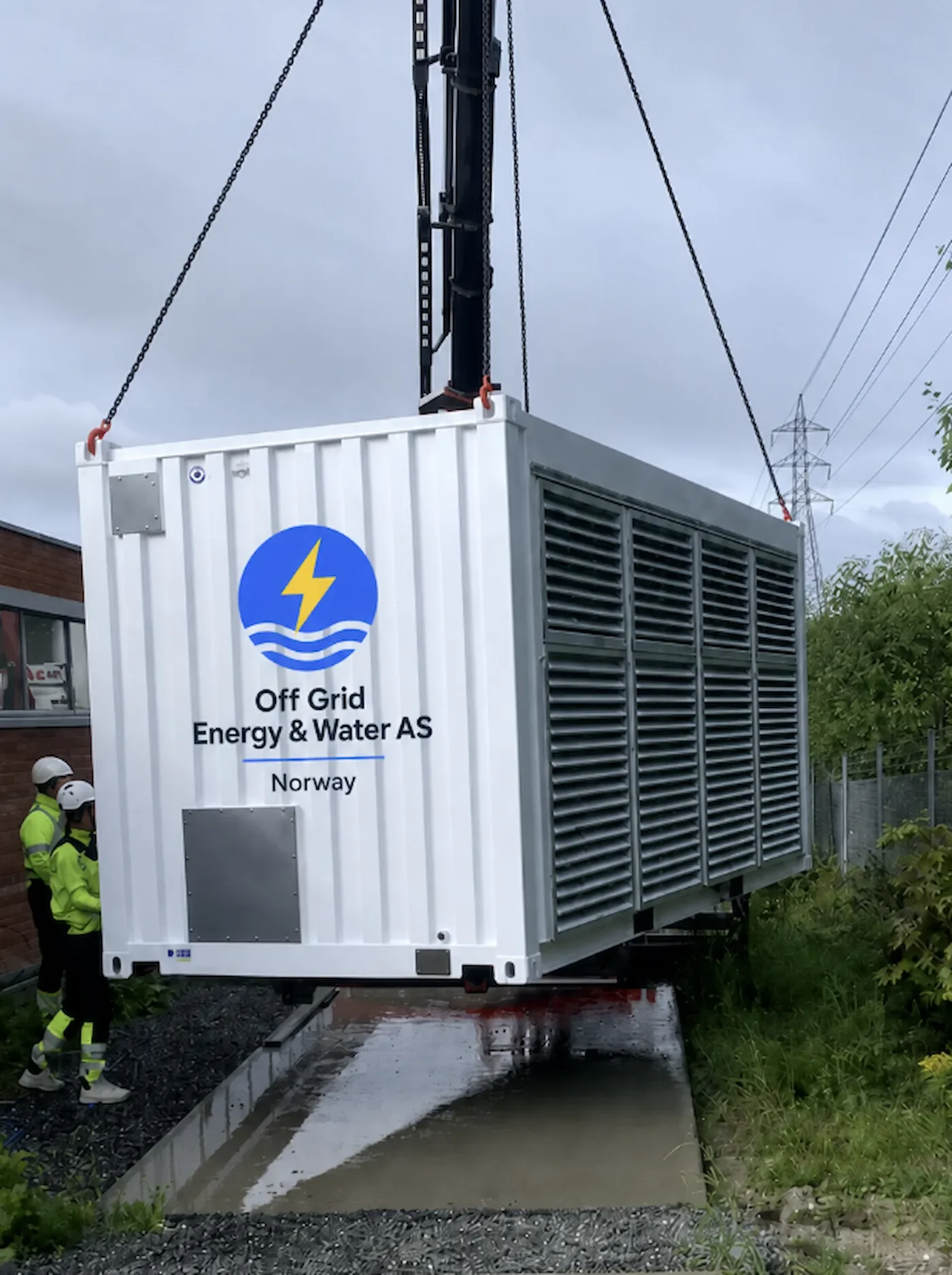 A large off-grid energy and water generator being installed outdoors, with workers in safety gear nearby.