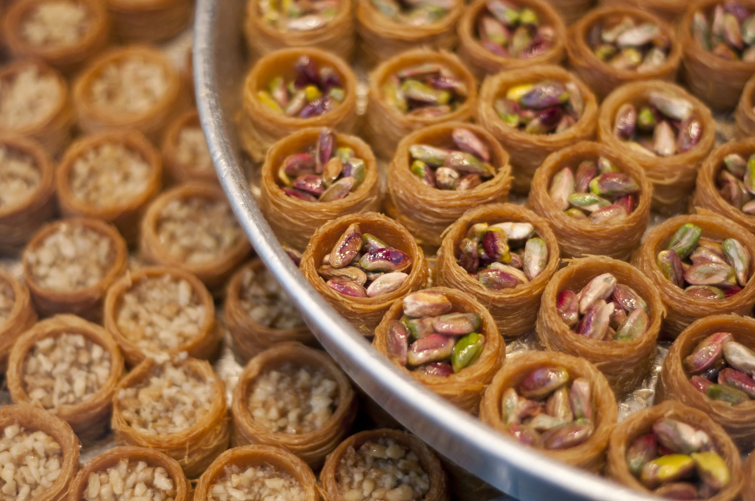 Tray filled with small round baklava pieces, some topped with pistachios.