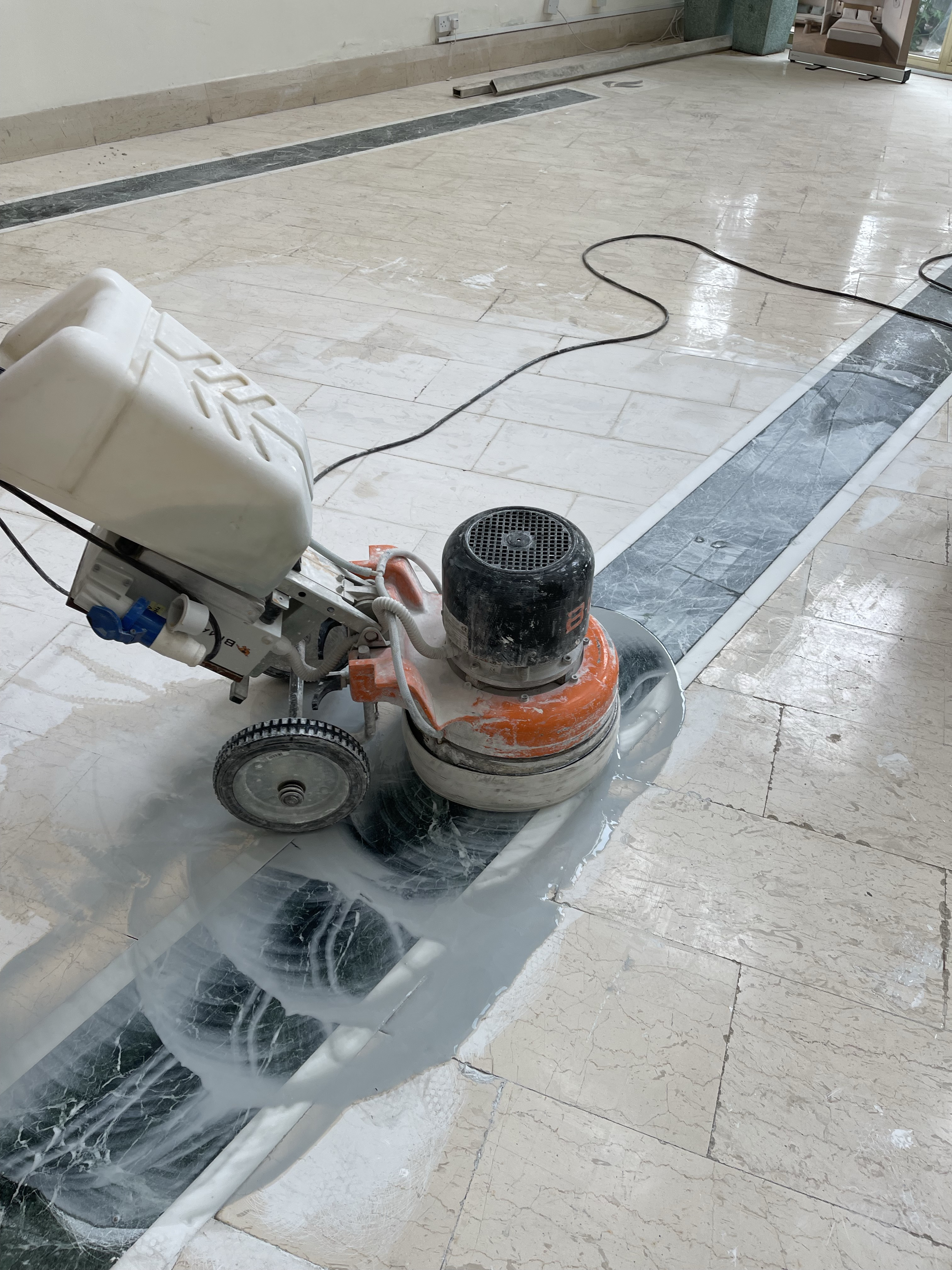 A floor polishing machine in use on a marble floor, with some areas still wet and others dried and shiny.