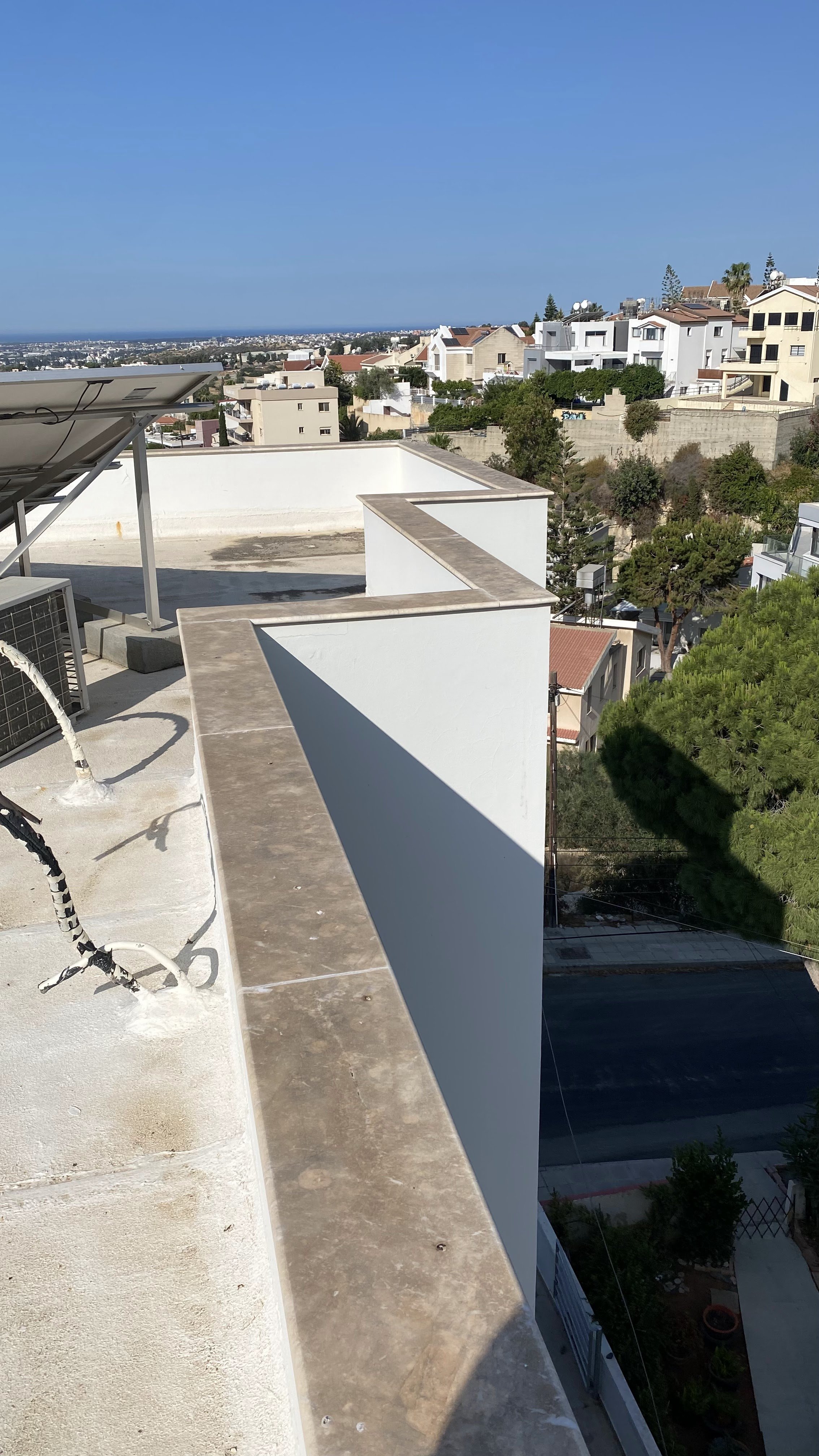 Balcony on a high-rise building overlooking a suburban neighborhood with various houses, trees, and a distant view of the horizon under a blue sky.