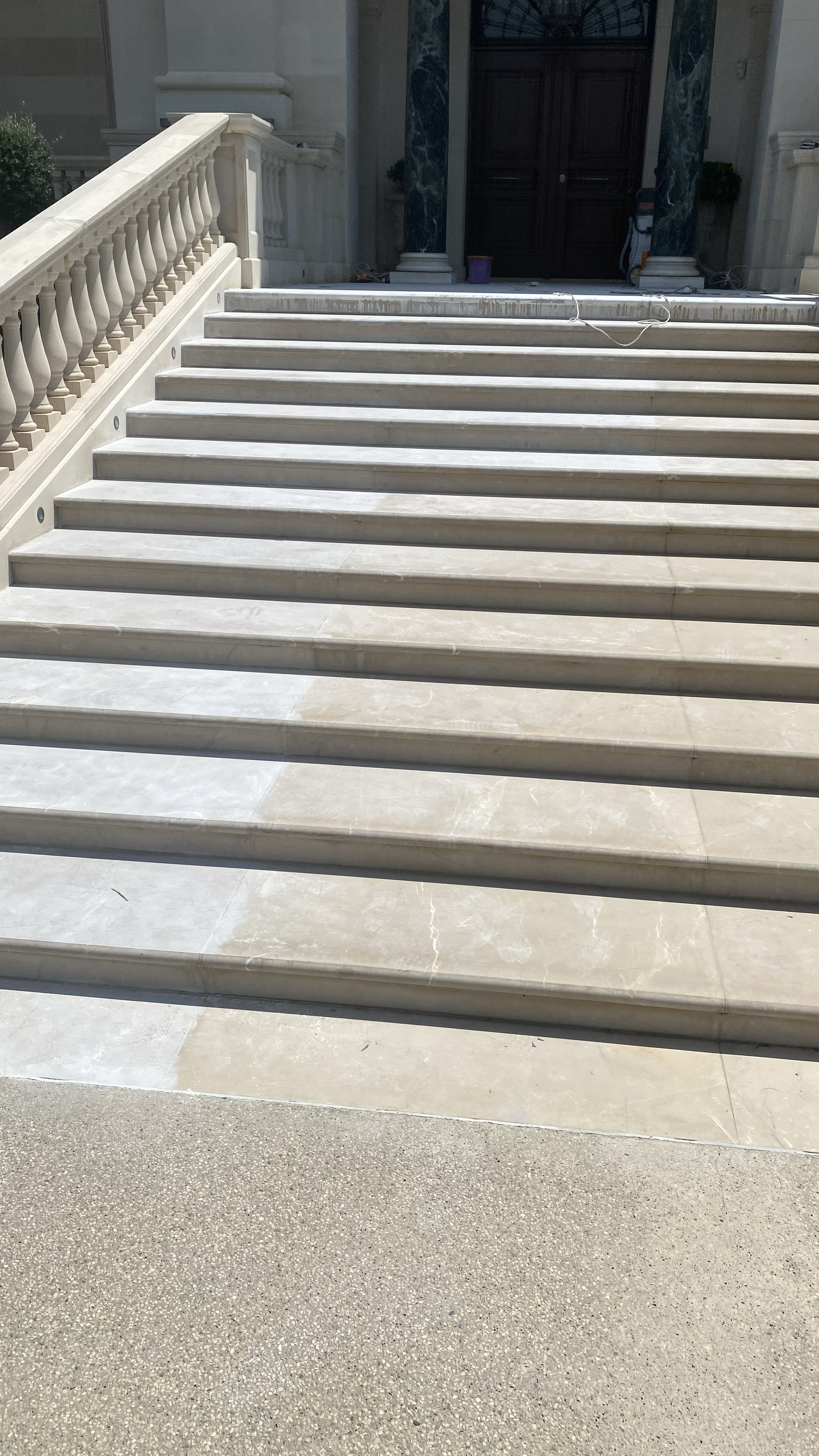 A set of marble stairs leading up to a building entrance with dark double doors, marble columns, and a railing on the left side.