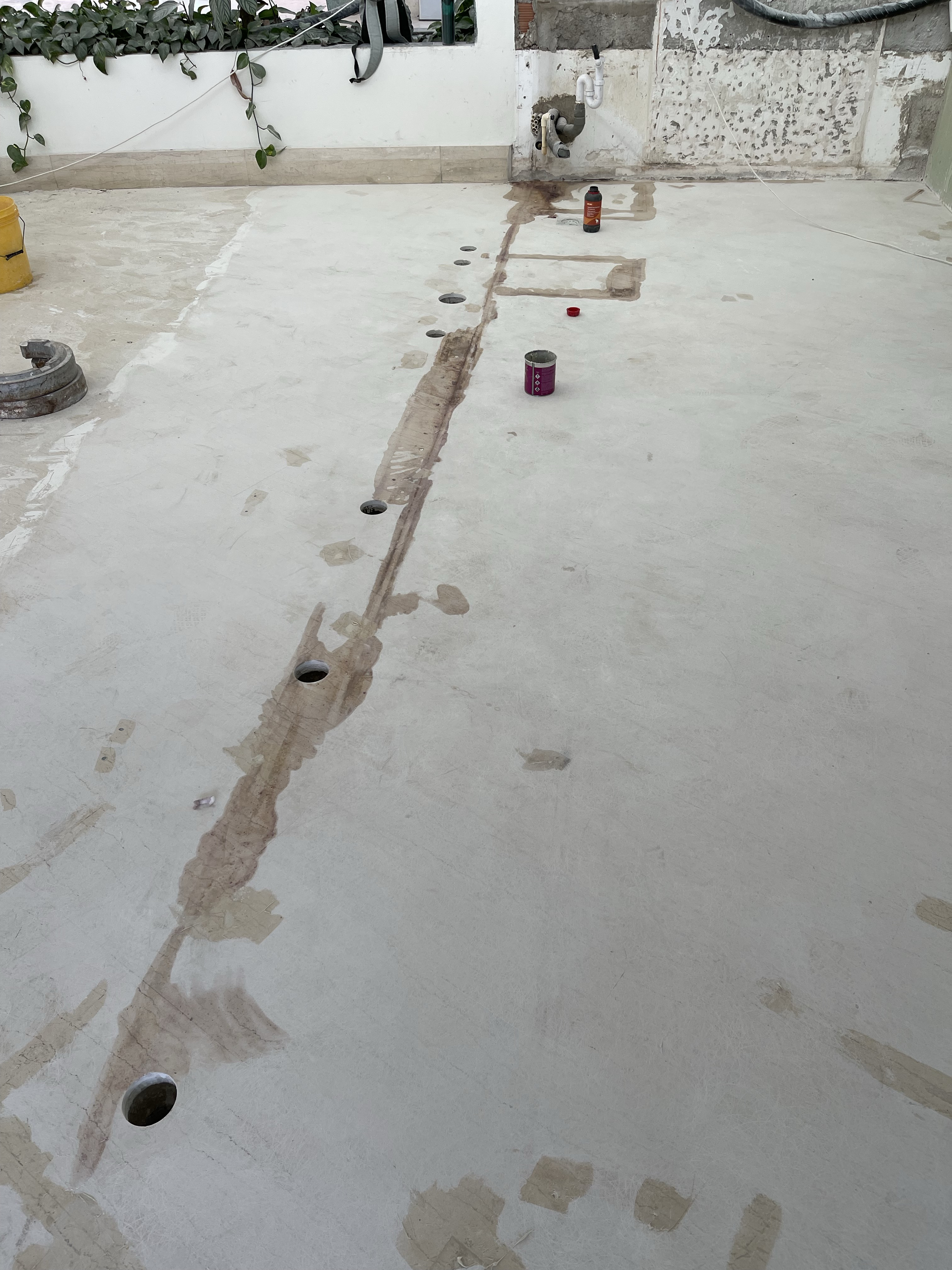 Construction site with a freshly laid concrete floor, visible plumbing pipes, and tools.