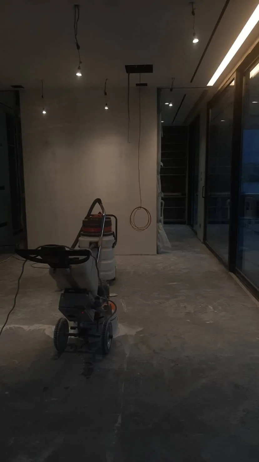 An unfinished room with exposed hanging light bulbs, a vacuum cleaner, and construction materials, with a sliding glass door to the right.