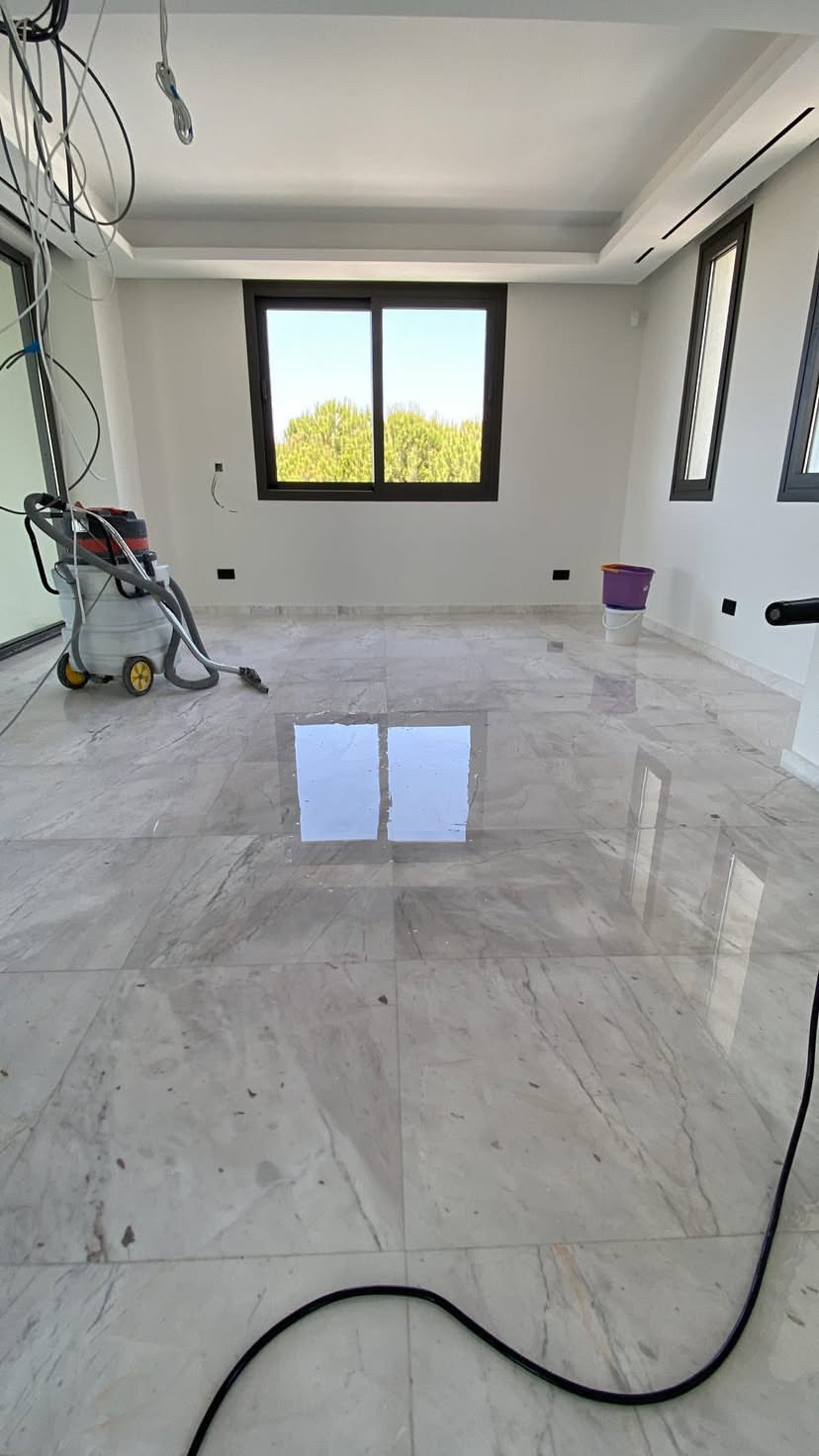 Empty room under construction with marble flooring, windows, and construction tools and wires present.