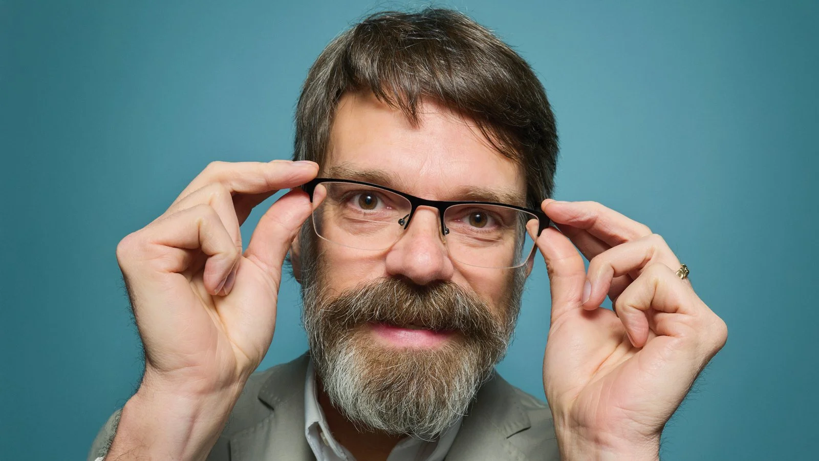 Prof C adjusting his glasses, posed against a plain blue background.