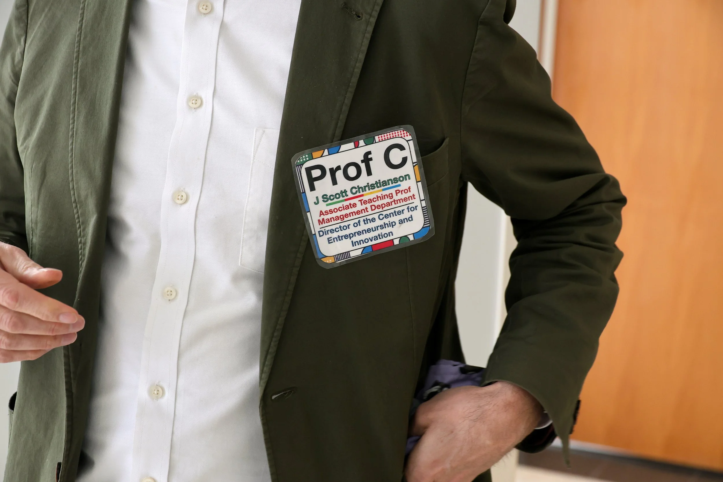 Close-up of a Prof C wearing a white button-up shirt and a dark blazer with a name badge that reads 'Prof C, J Scott Christianson, Associate Teaching Prof, Management Department, Director of the Center for Entrepreneurship and Innovation'.