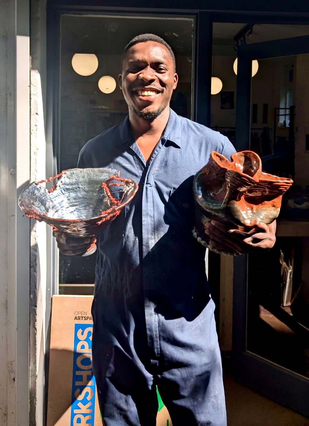 A man smiling and holding two handcrafted ceramic bowls outside a shop.